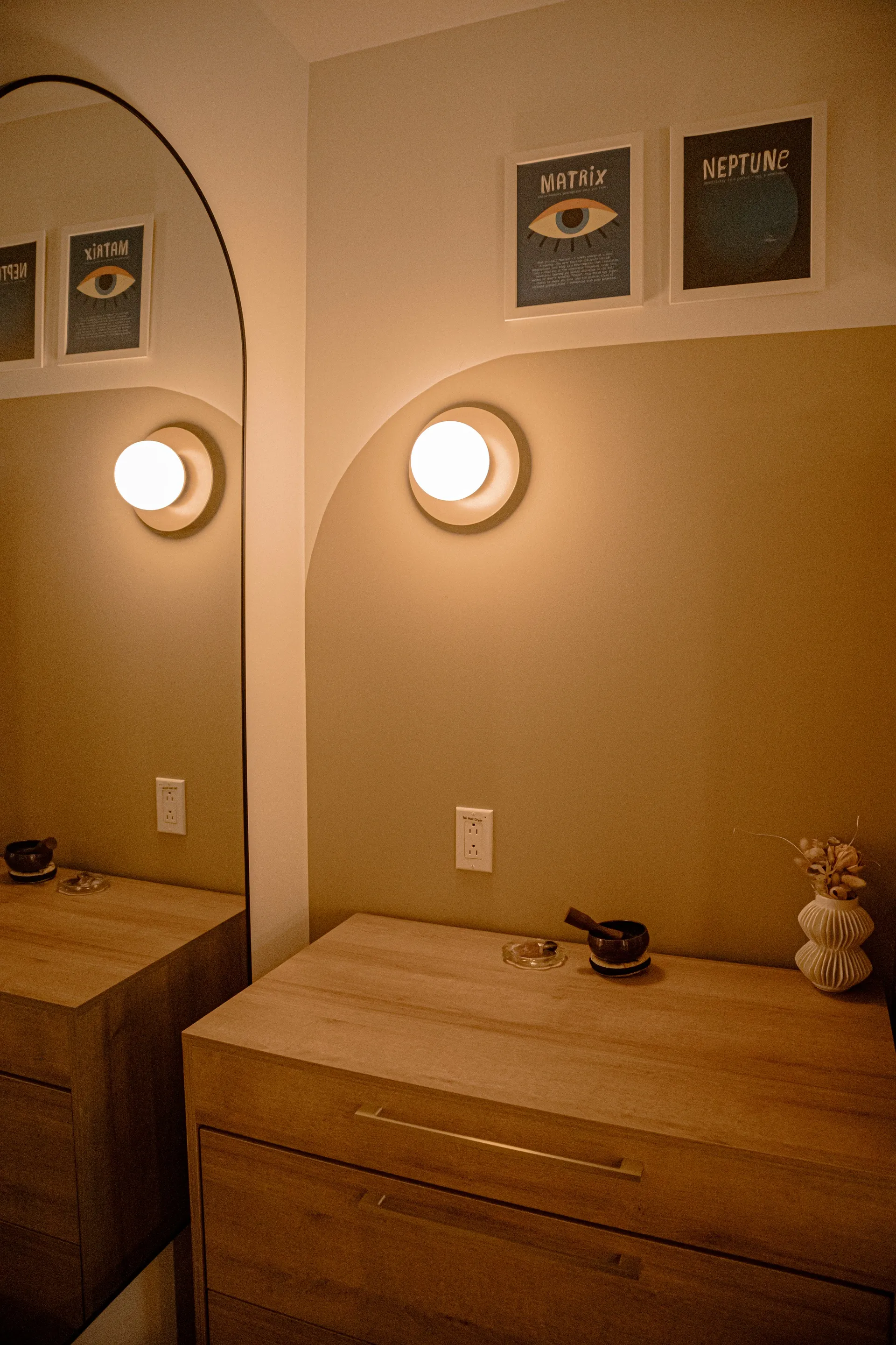 Oak dresser with a singing bowl and dried flowers beneath framed astrology prints in a warmly lit Ralia room
