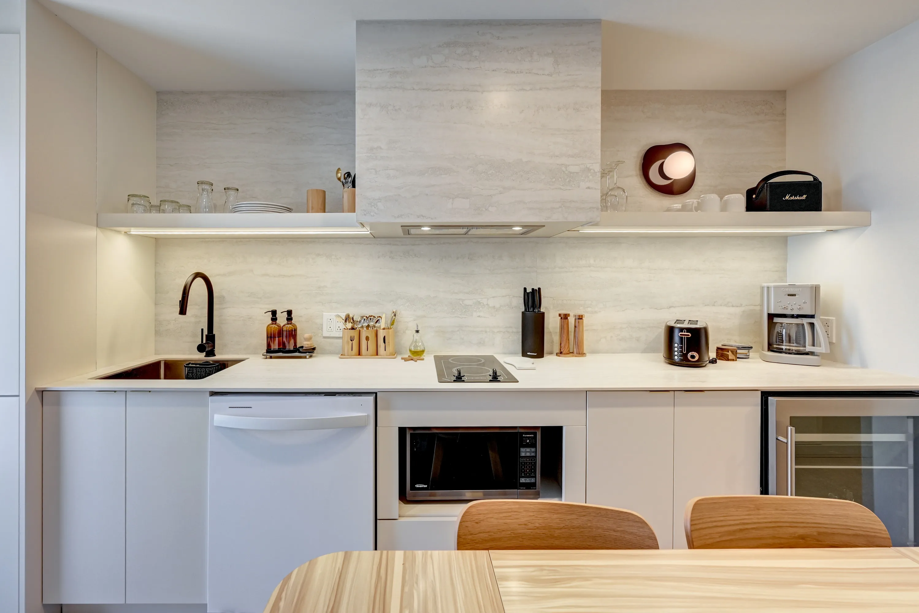Bright kitchenette with stone backsplash, cooktop and wood dining table in a La Maison Ralia apartment