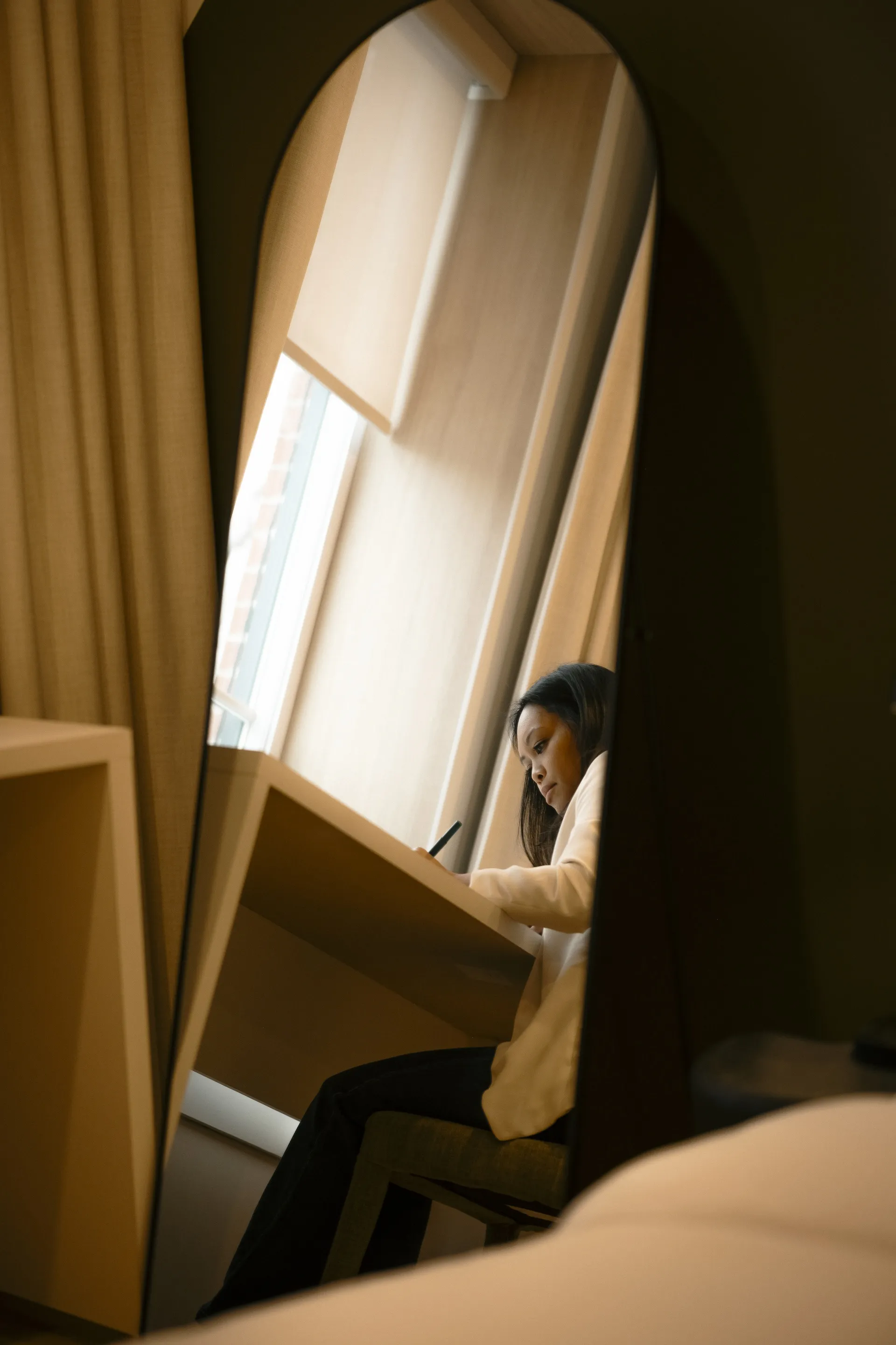 A guest writing at a desk by the window, reflected in an arched mirror in a Ralia guest room