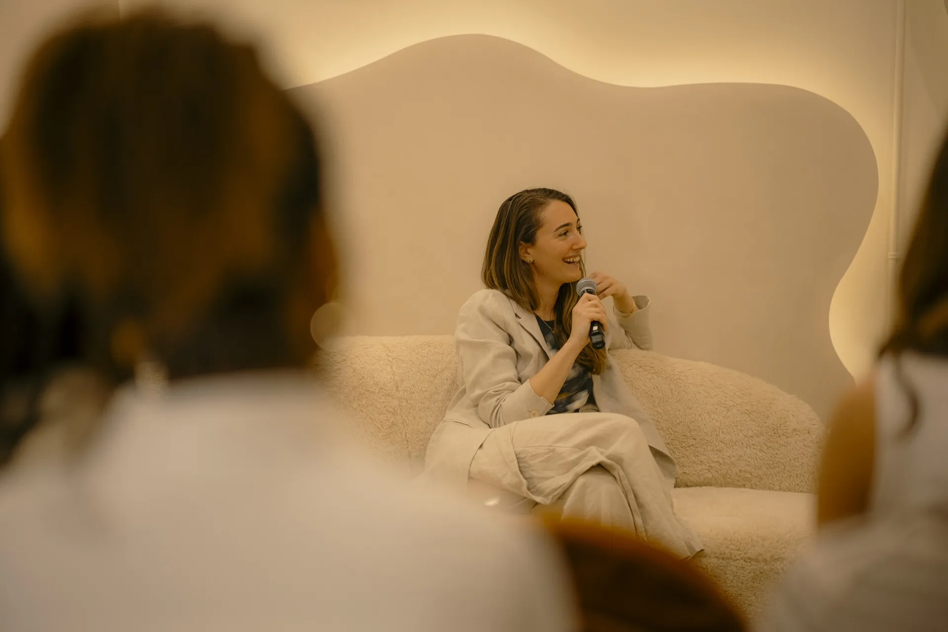 Speaker with a microphone on a cream sofa addressing guests in the Connections event space at La Maison Ralia
