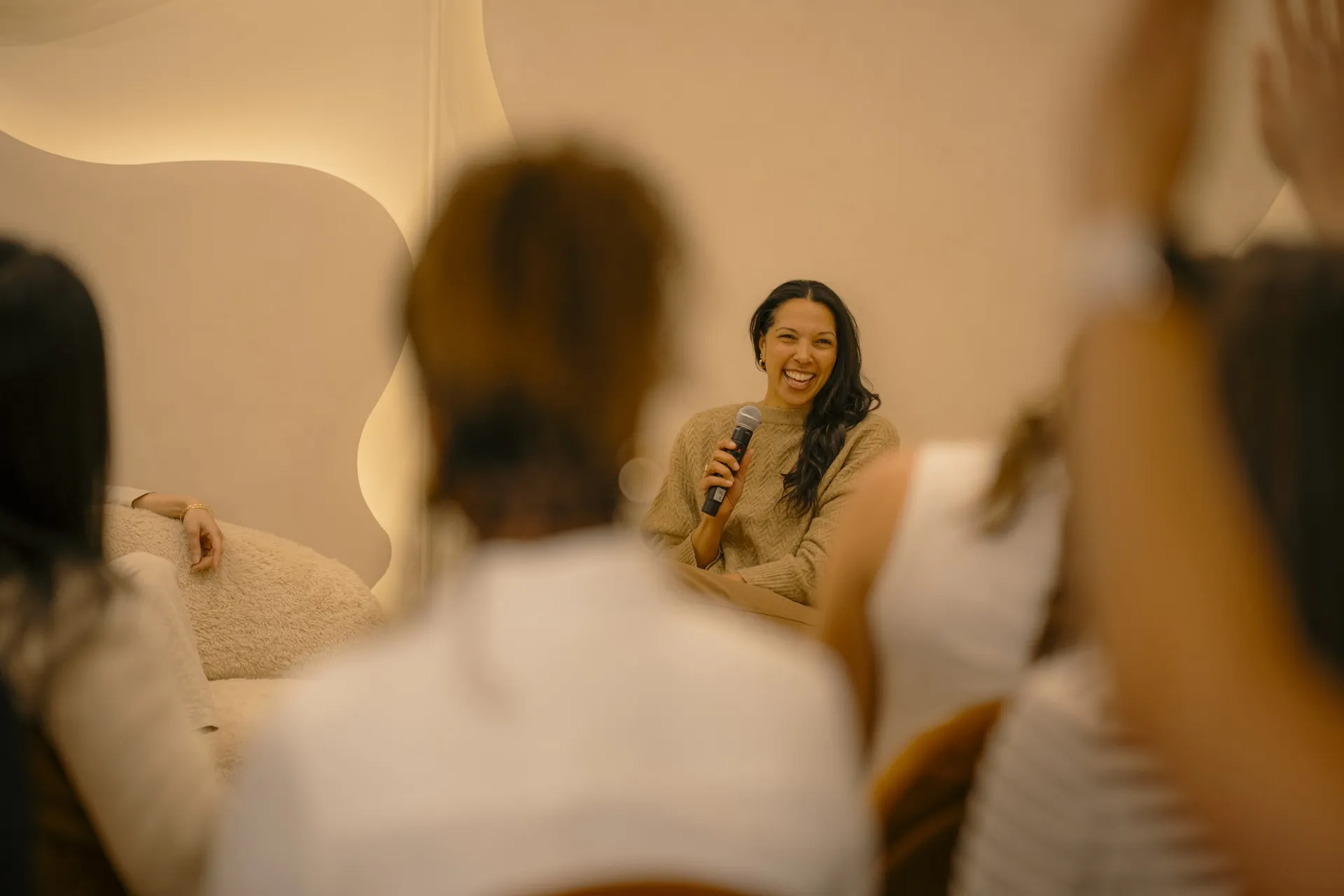 Speaker laughing with a microphone as guests listen during a group session at La Maison Ralia Montreal