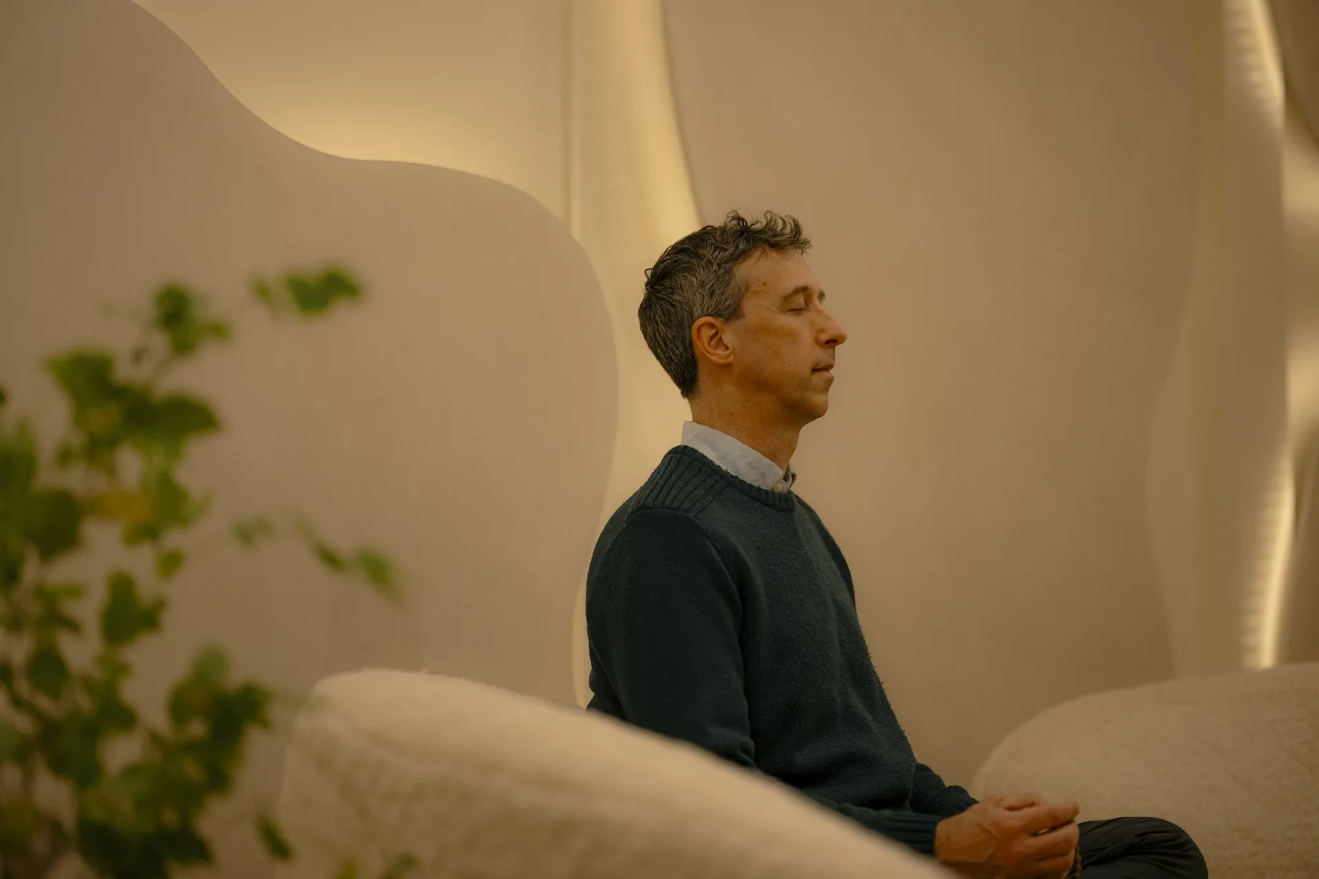 Man meditating with eyes closed on the curved white banquette in the Connections space at La Maison Ralia