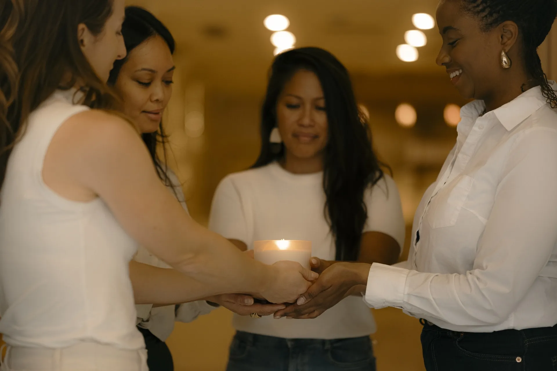Four women holding a lit candle together in a circle during a Ralia retreat gathering