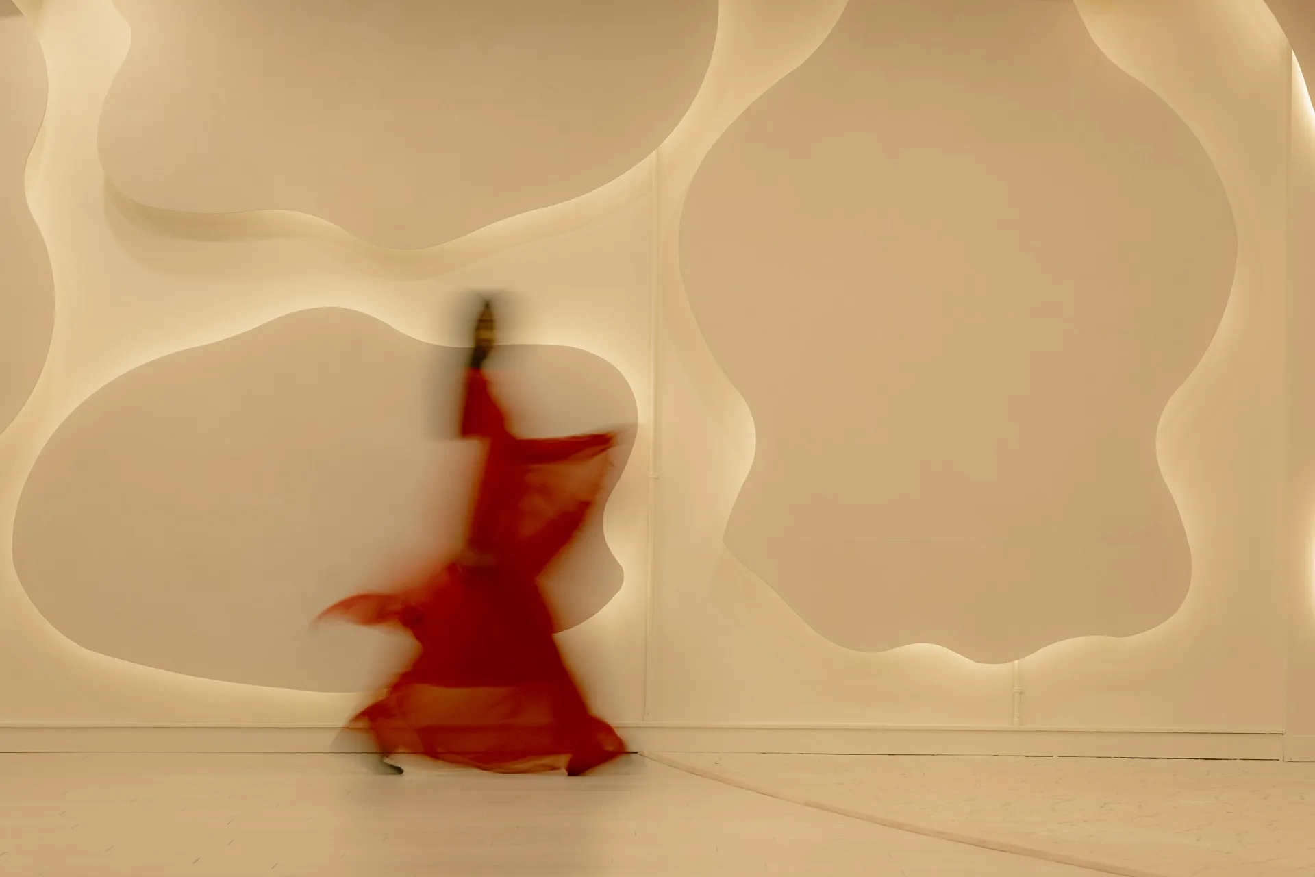 A dancer in a flowing red dress moving against the sculpted wavy white wall of the Connections event space