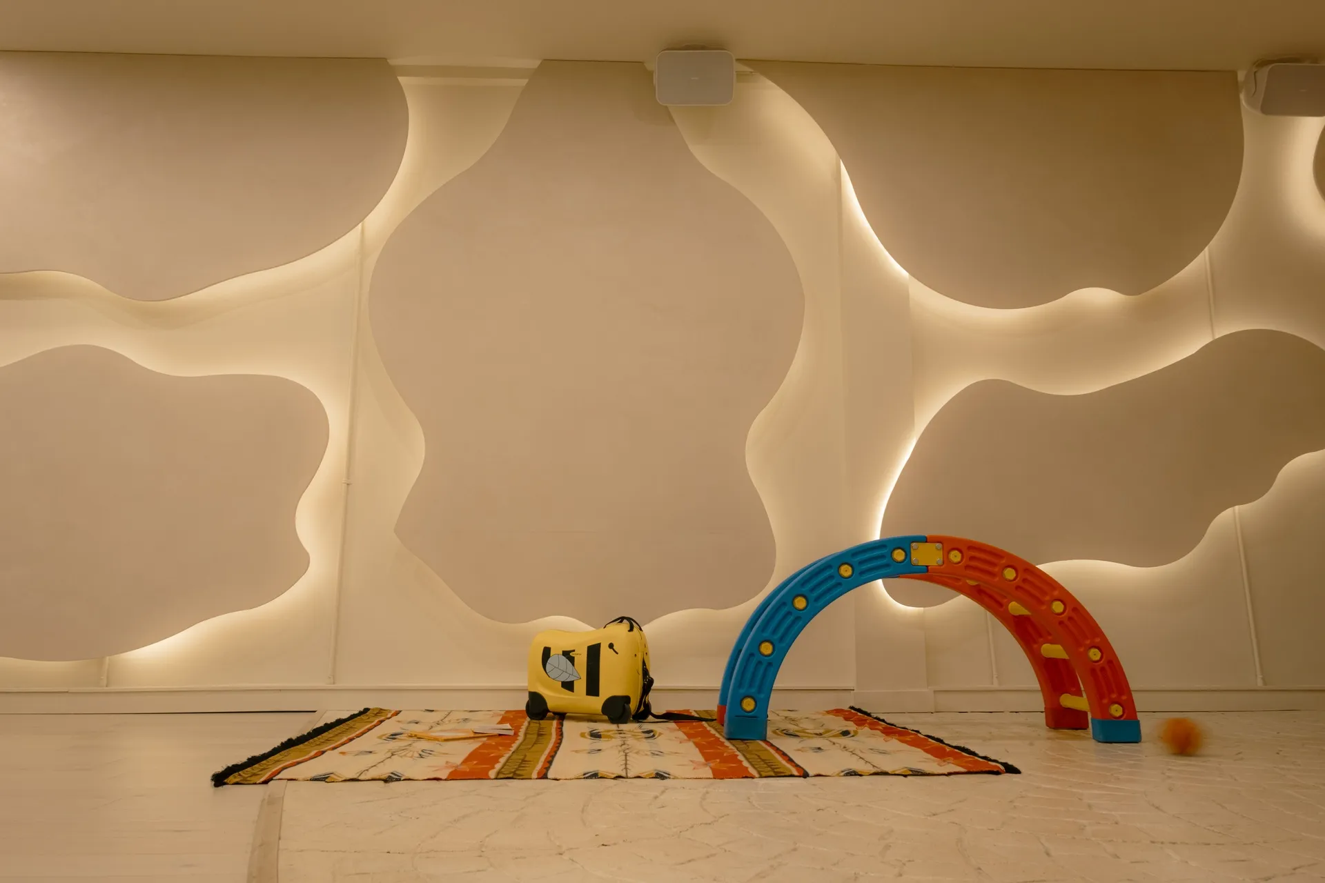 Toy car and rainbow arch on a striped rug beside the sculpted wavy wall in the Connections event space