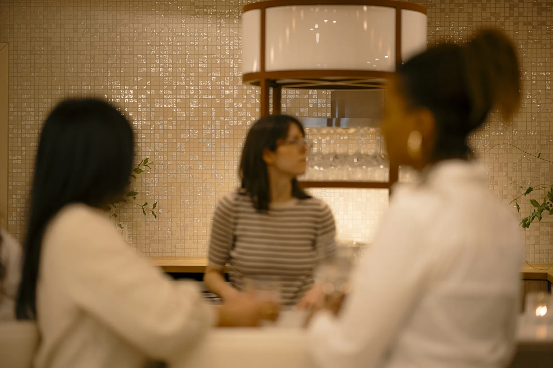 Three guests talking over drinks at the bar beneath a large drum pendant light at Ralia