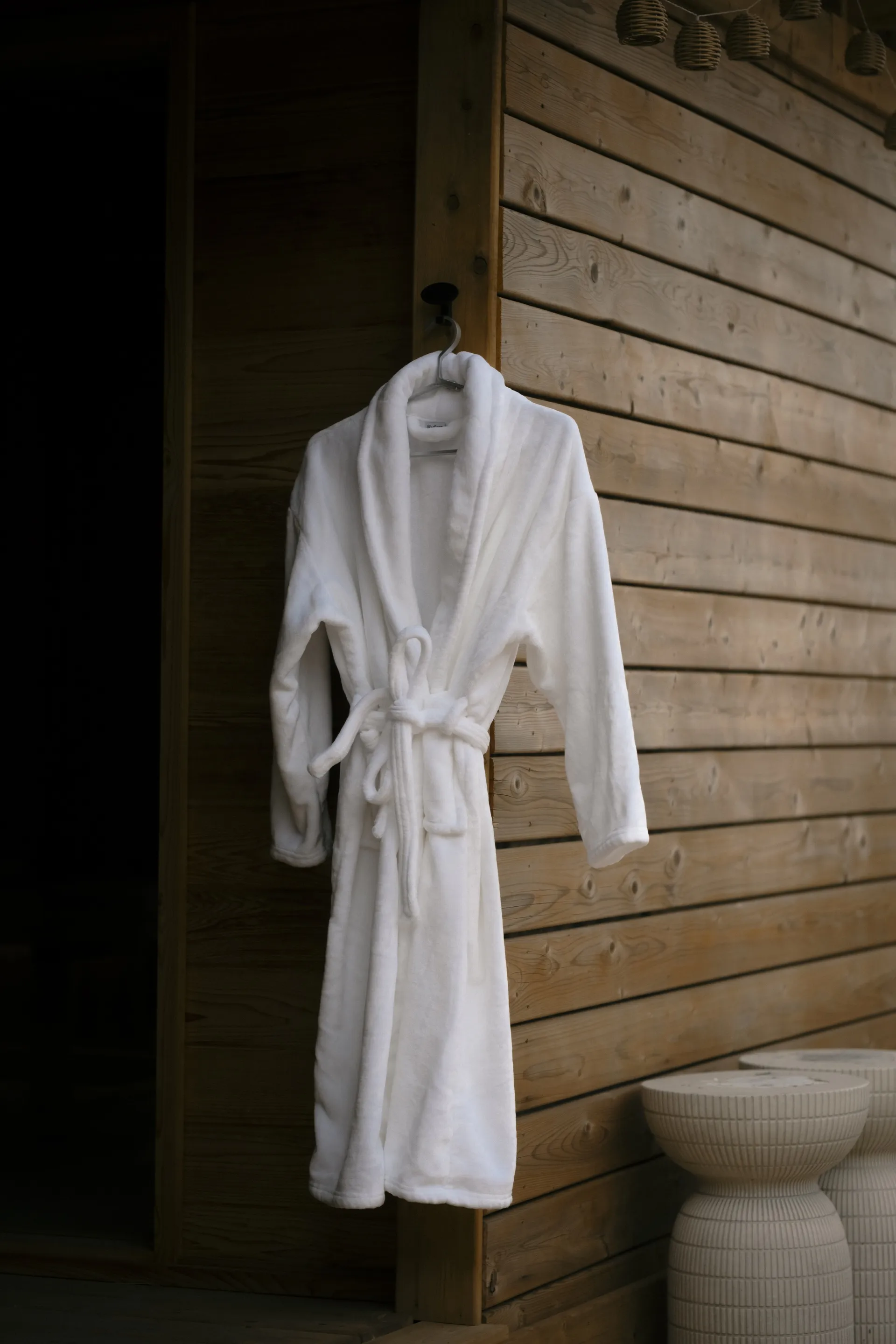 White bathrobe hanging on a cedar-panelled wall beside a fluted side stool