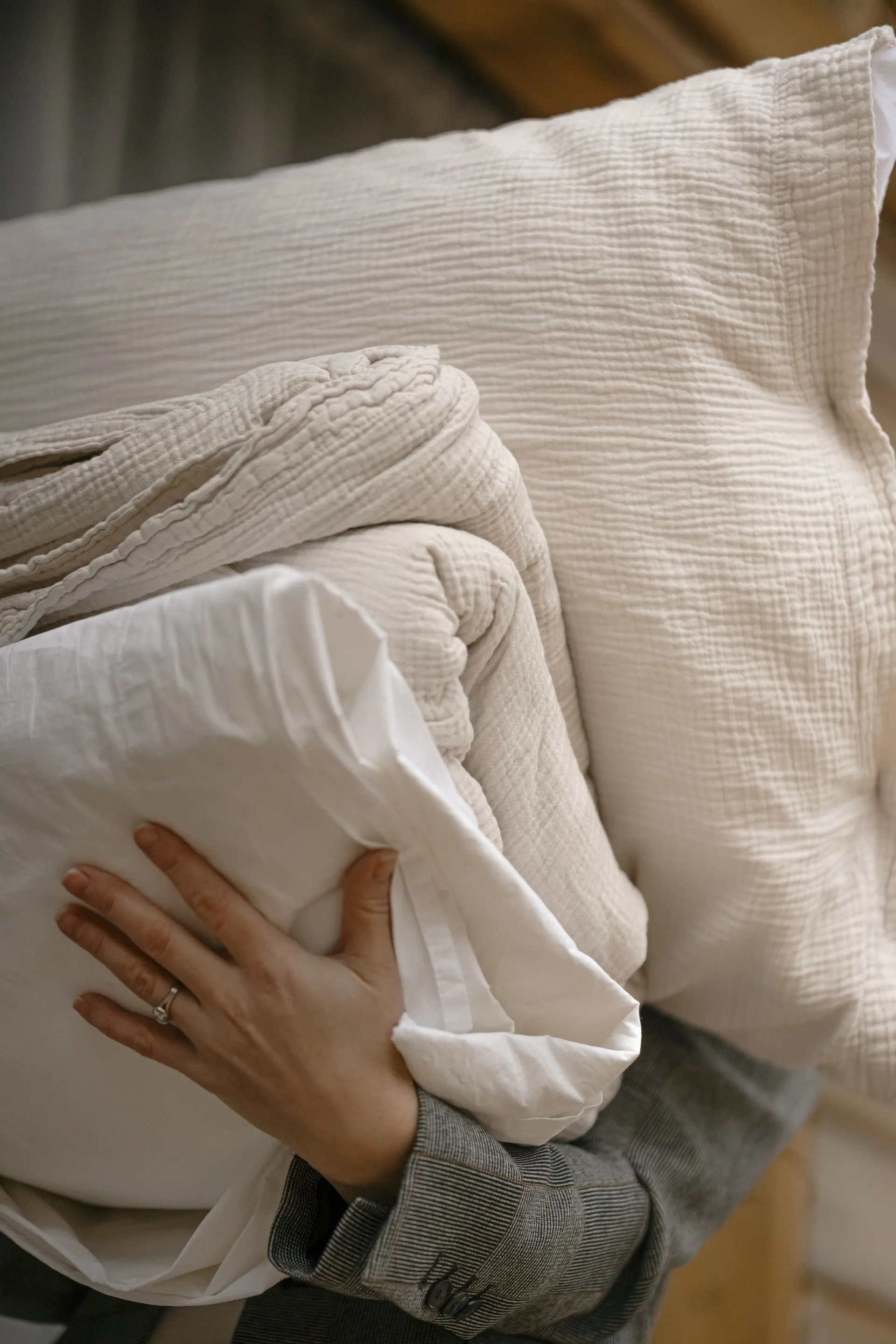 Hands carrying a folded stack of ivory cotton bedding and pillows from the Ralia boutique