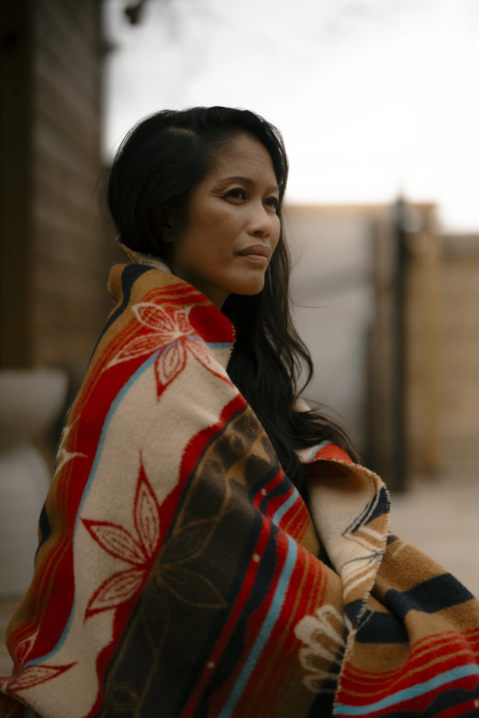 Woman wrapped in a patterned wool blanket outdoors in soft evening light