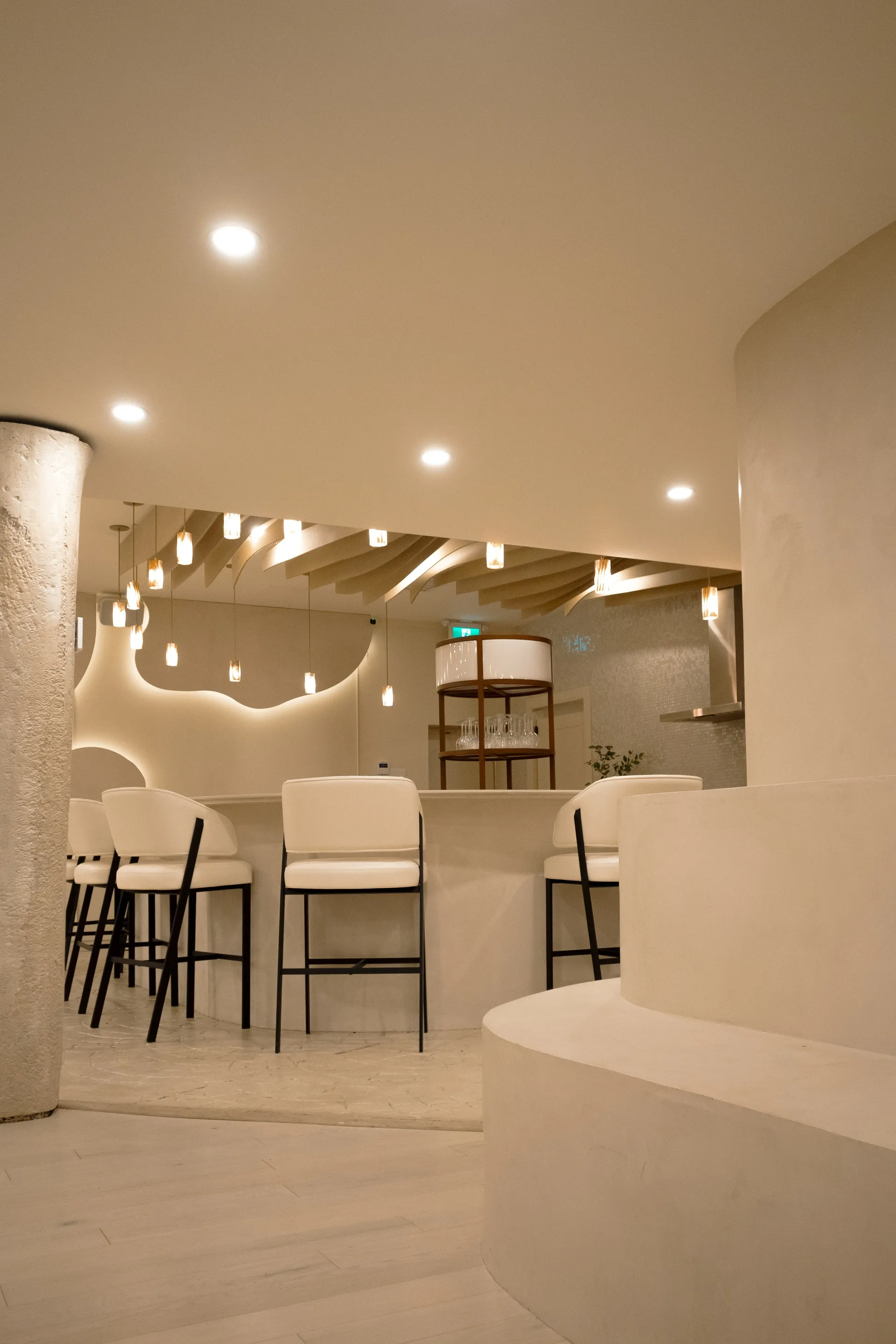 Curved white bar with upholstered stools and glass pendant lights in the Connections event space at La Maison Ralia