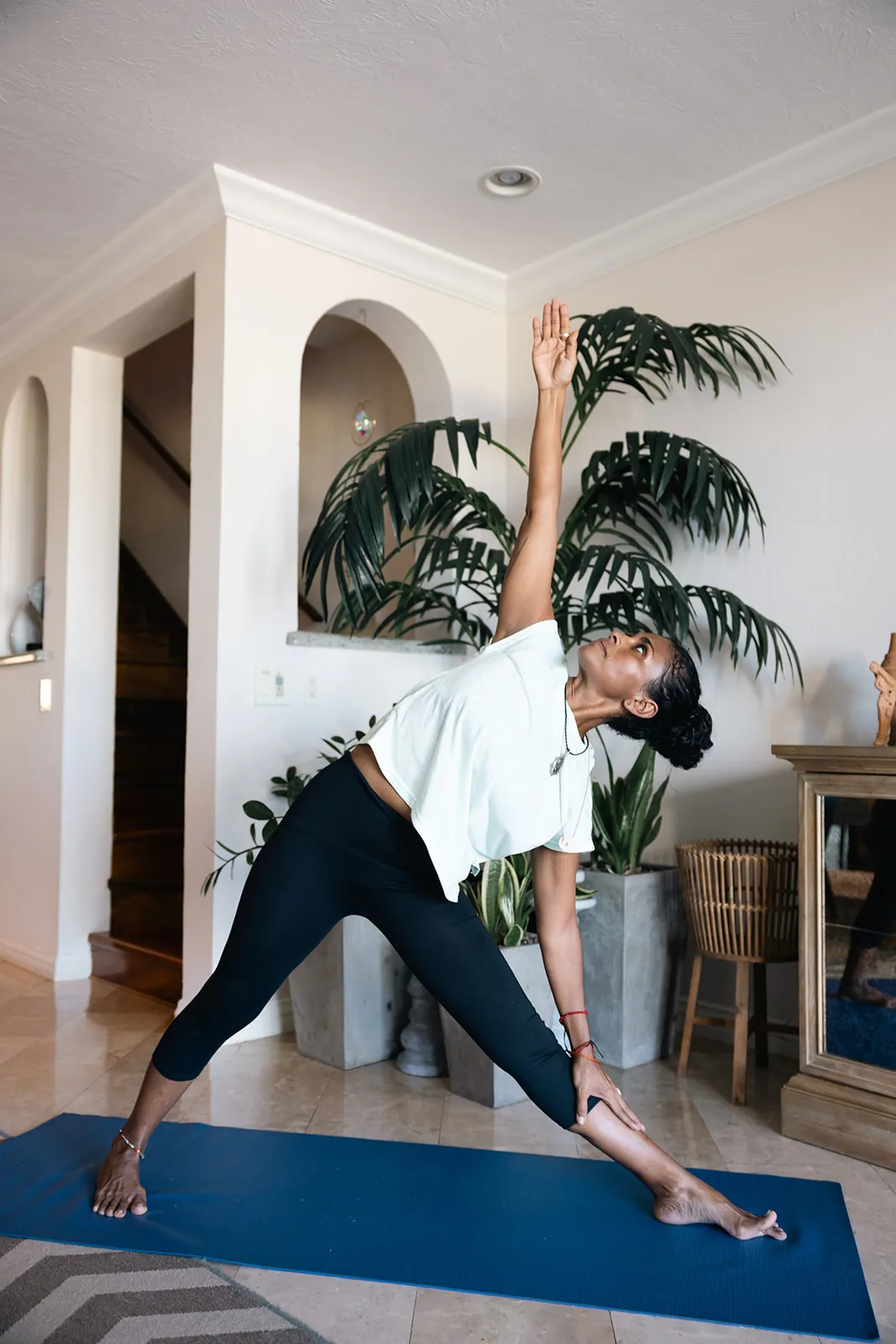 Guest holding a triangle pose on a yoga mat in the villa's plant-filled living room