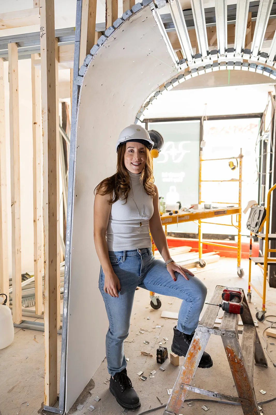 Woman in a hard hat resting on a ladder beside a curved archway during the Ralia build