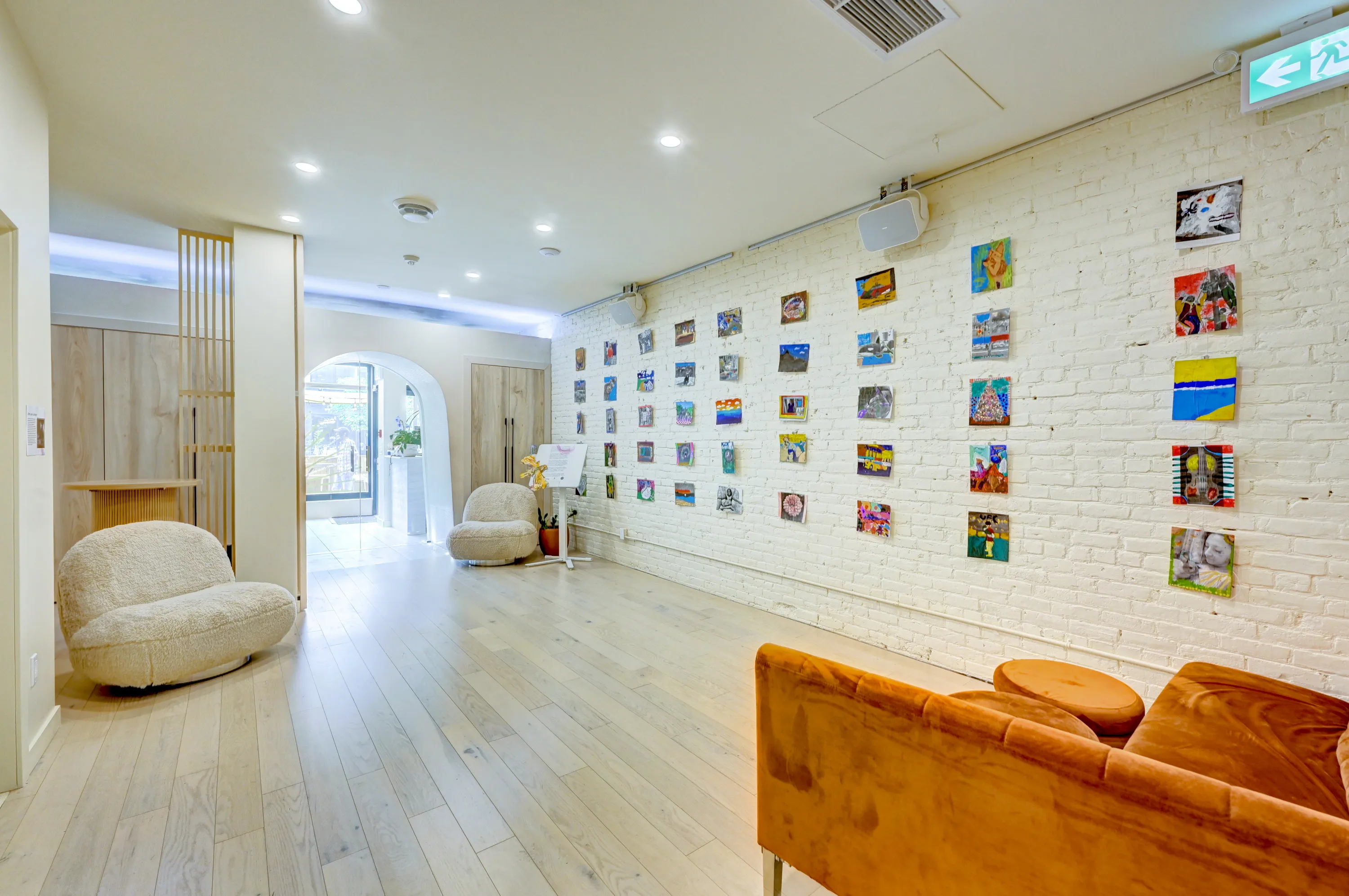Bright lounge corridor with small artworks on a white brick wall, boucle chairs and a tan leather sofa