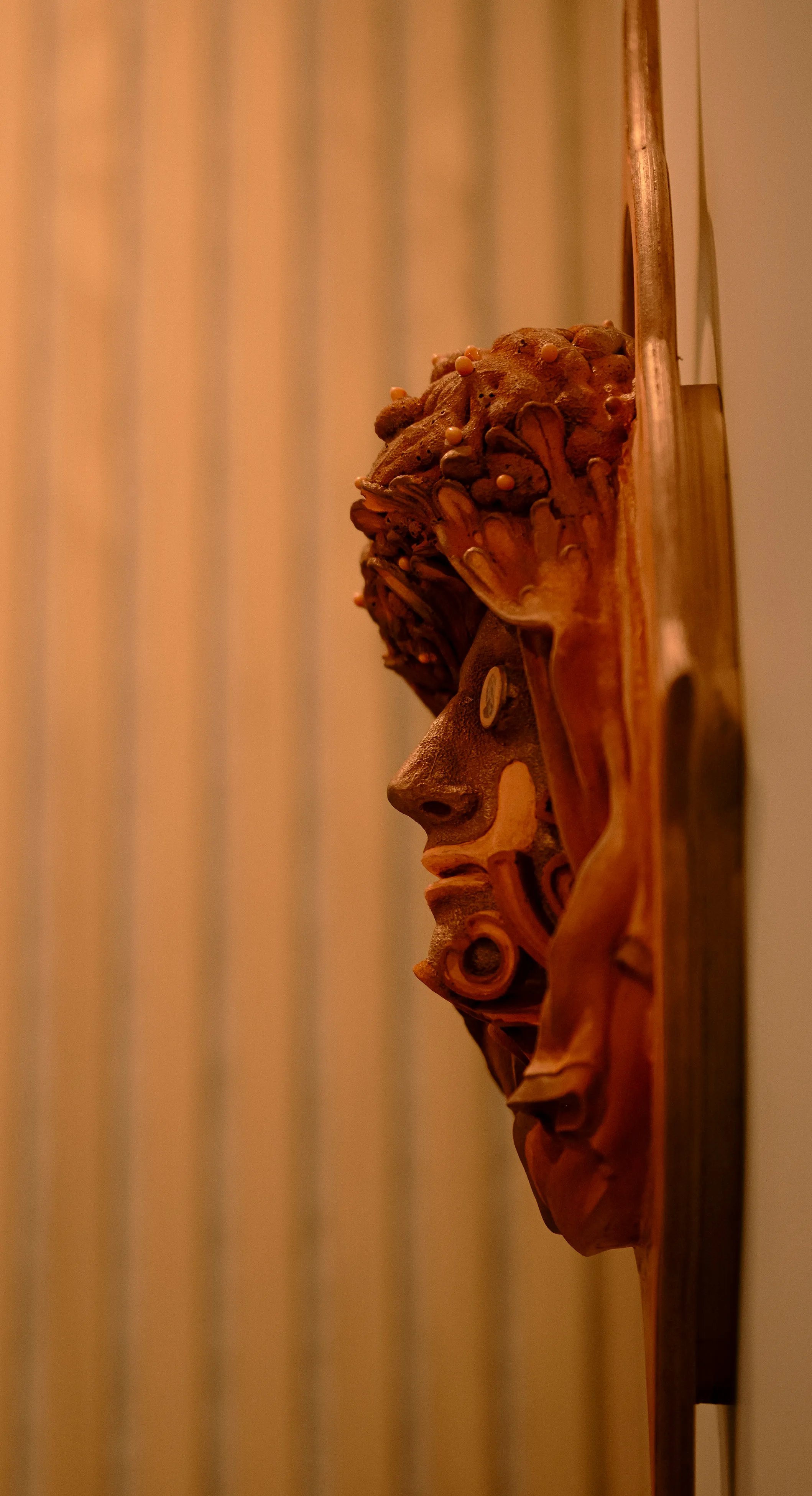 Carved wooden face sculpture mounted on a wall in a warmly lit corner at Ralia