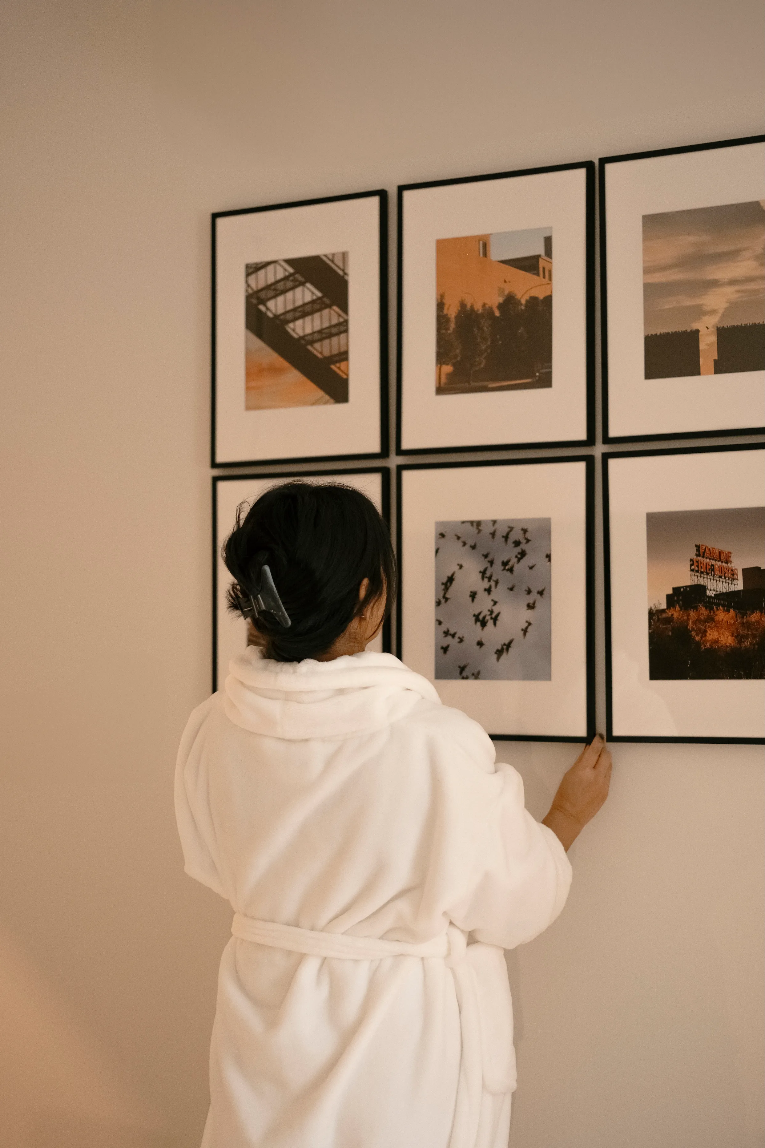 A guest in a white robe adjusting framed photographs on a gallery wall at Ralia