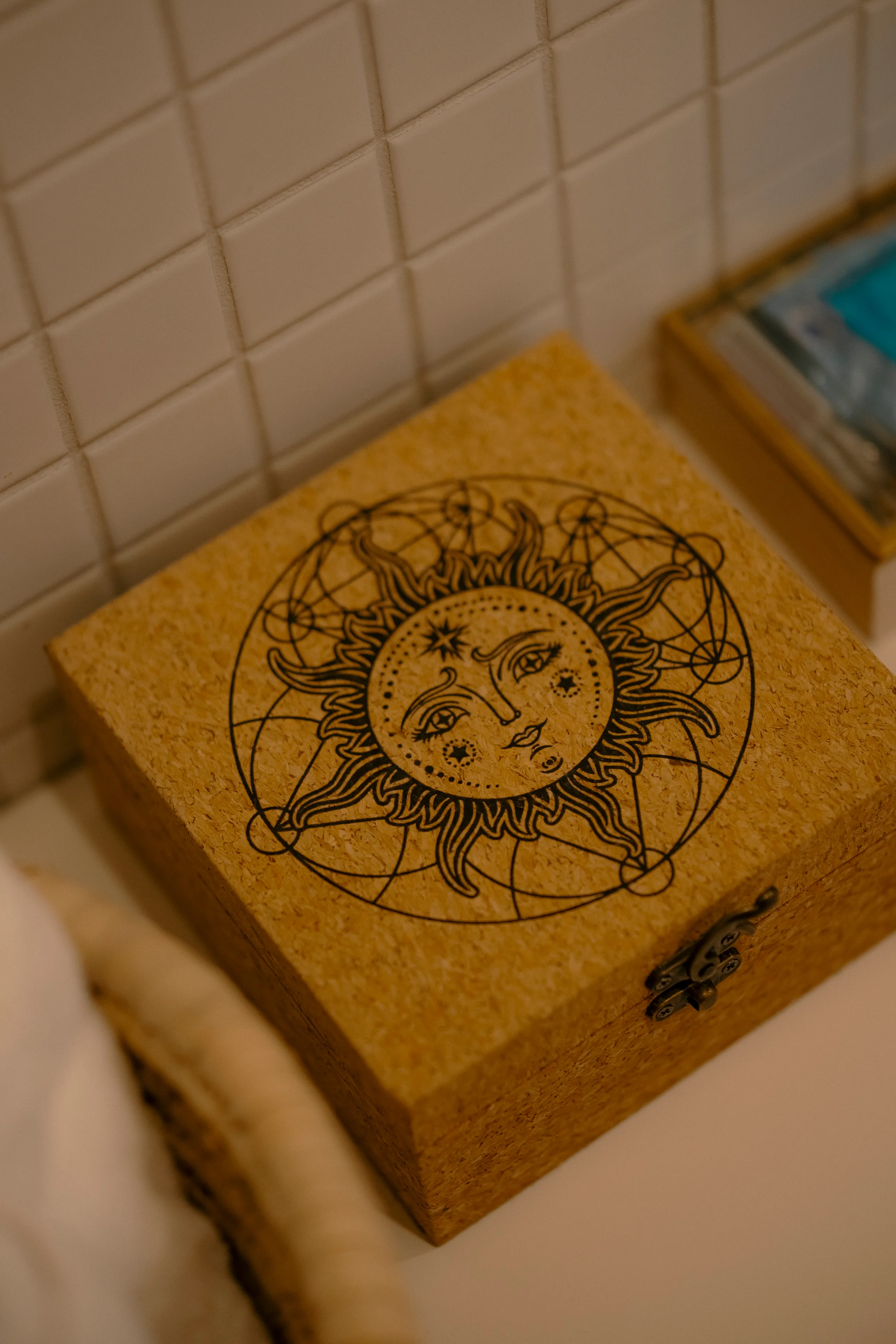 Wooden box engraved with a sun and moon celestial design resting on a tiled bathroom counter