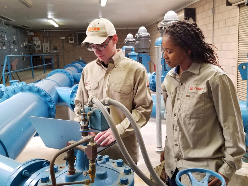 EMASS technician and a site operator are reviewing diagnostics on a laptop inside a pump station.