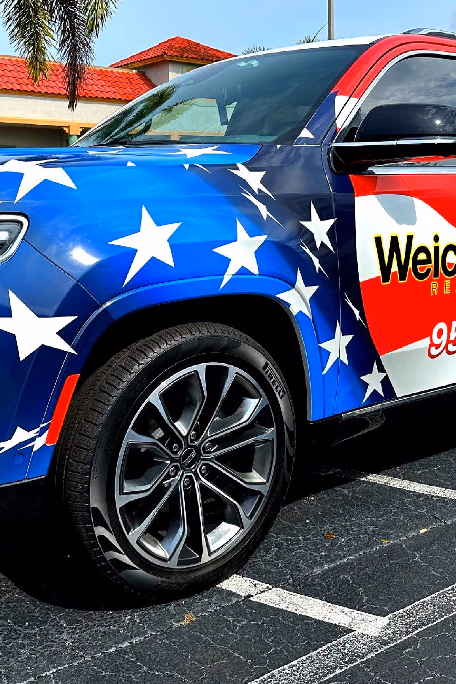 Front side of a car with a blue and red stars-and-stripes patriotic paint design parked on asphalt.