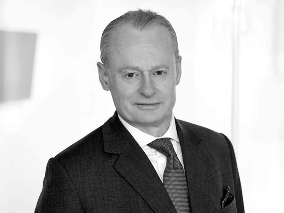 Portrait of a middle-aged man in a dark suit, white shirt, and patterned tie, looking slightly to the side.