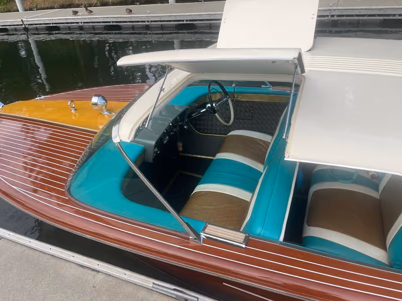 Vintage wooden boat docked, showcasing turquoise and brown cushioned seats with white striped accents under a white canopy.