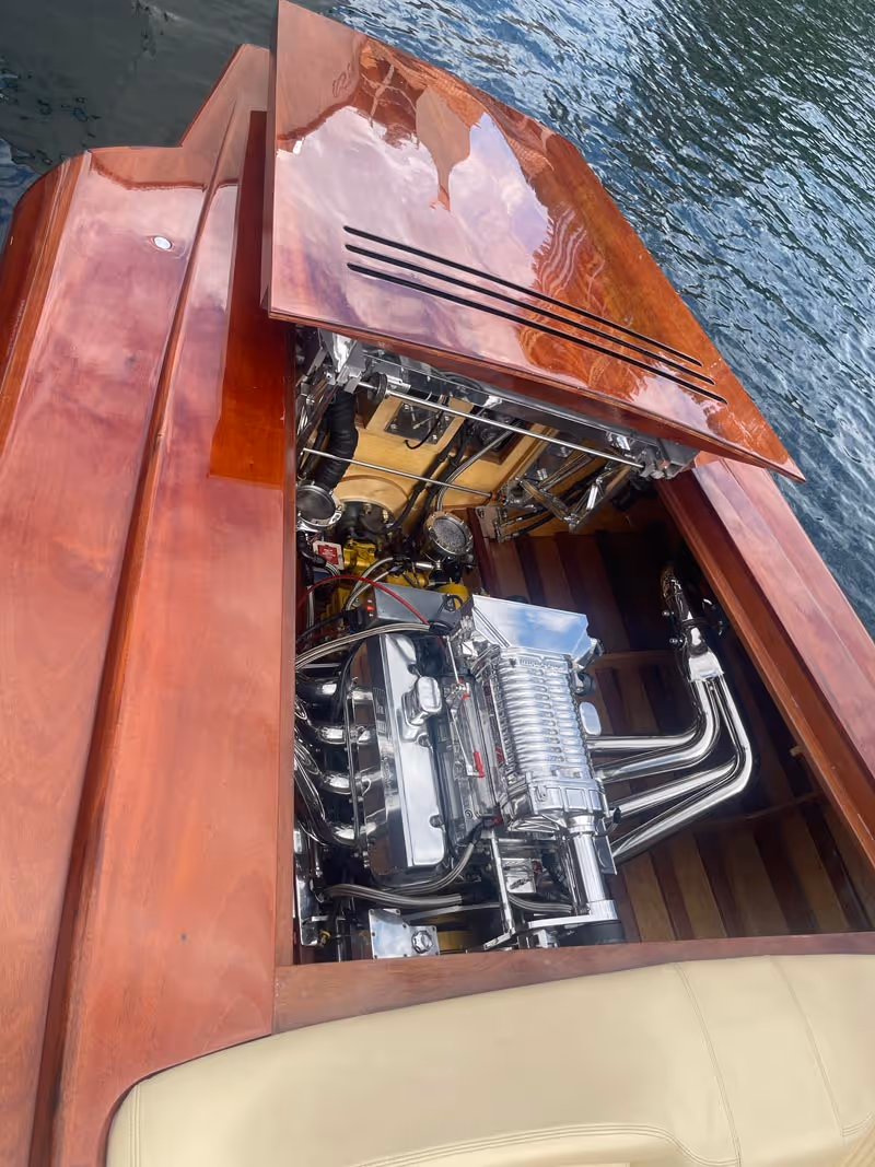 Polished wooden boat with open engine compartment showing a shiny chrome and metal engine inside.