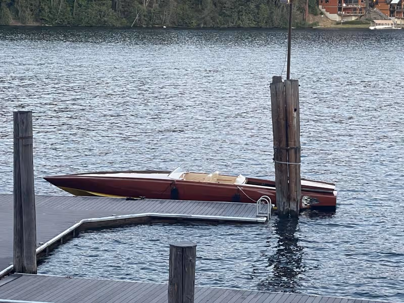 Maroon and yellow speedboat docked alongside a wooden pier on a calm lake.