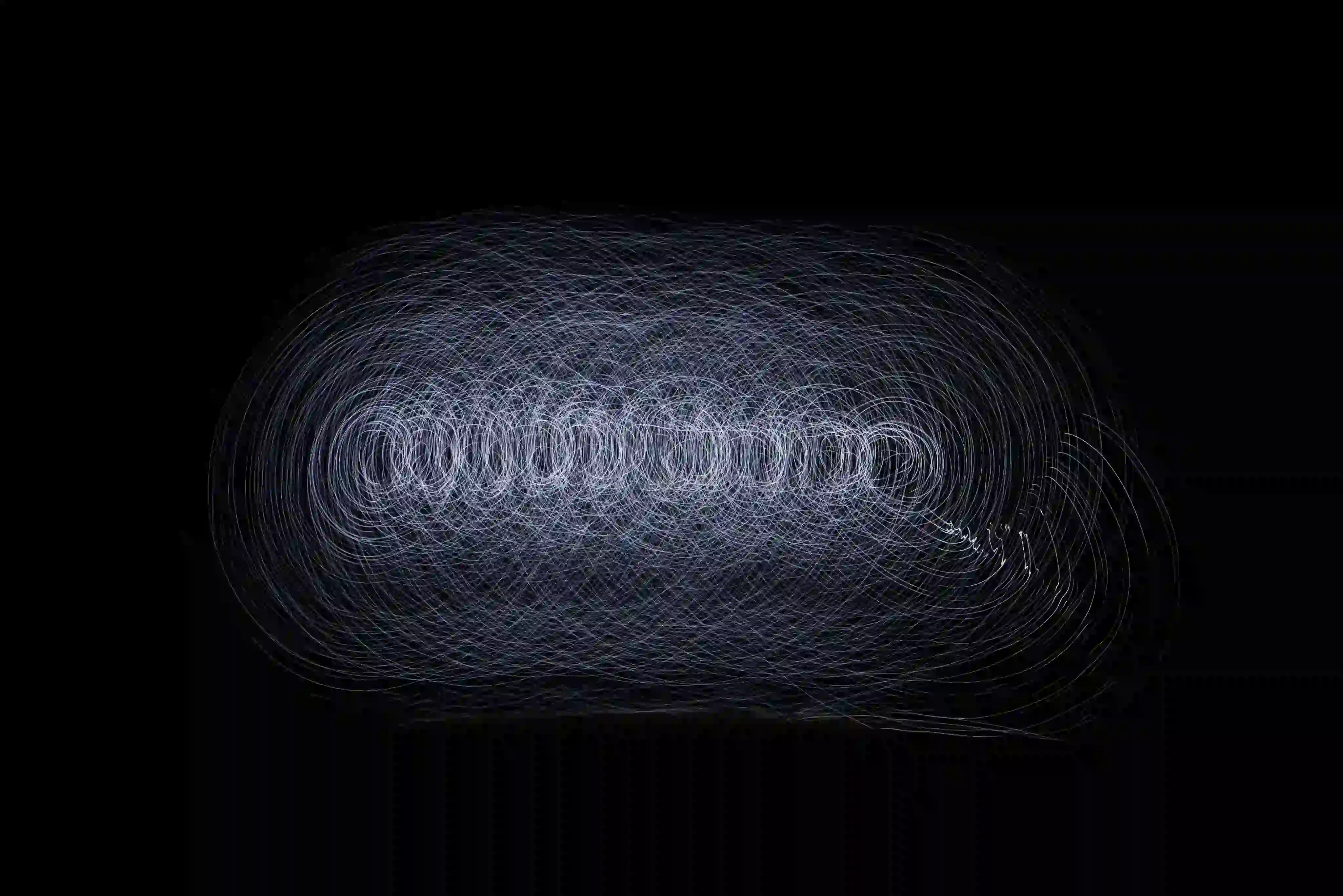 Long exposure light trails forming overlapping circular patterns on a black background.