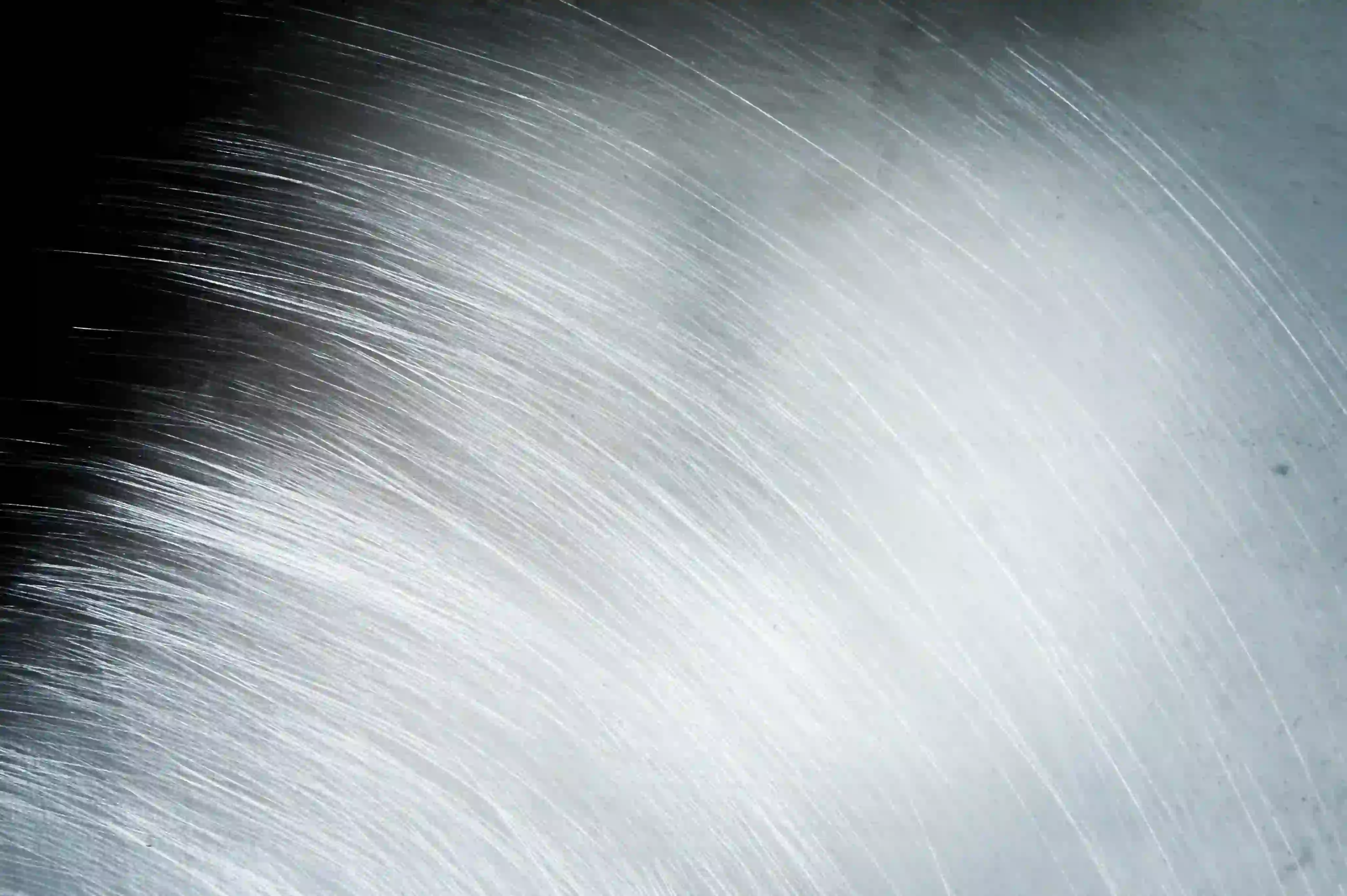 Close-up of a brushed metal surface with fine parallel scratches and a gradient from dark to light gray.