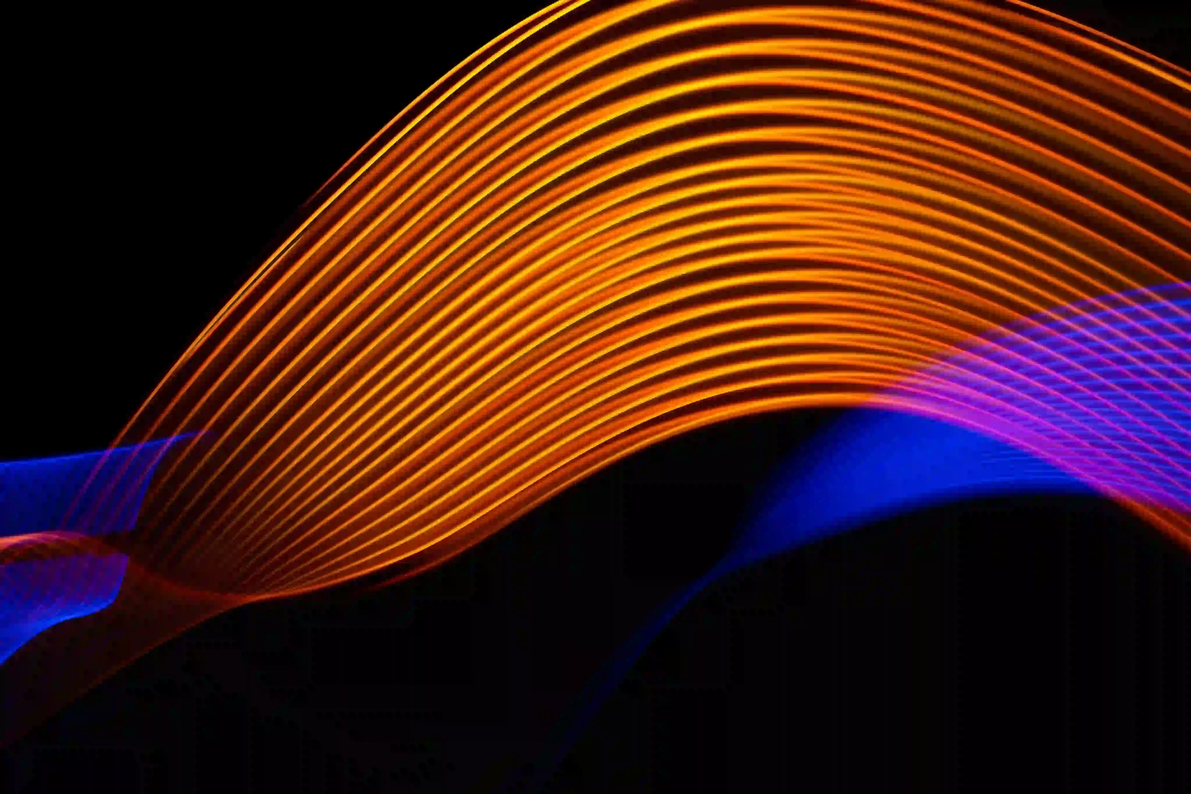 Abstract light trails of orange and blue waves against a black background.