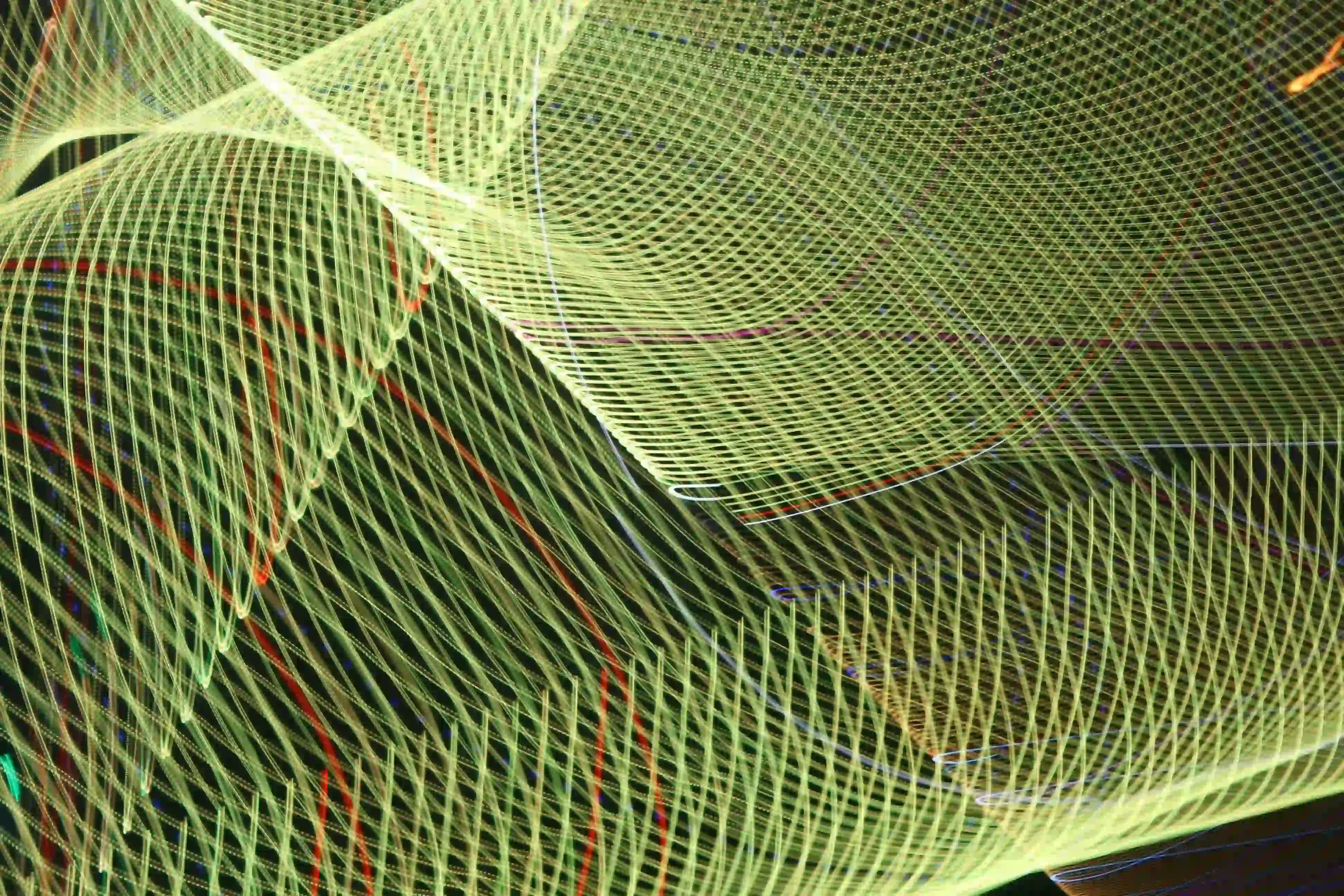 Abstract pattern of yellow-green light trails forming intricate, overlapping wave and grid shapes against a dark background.