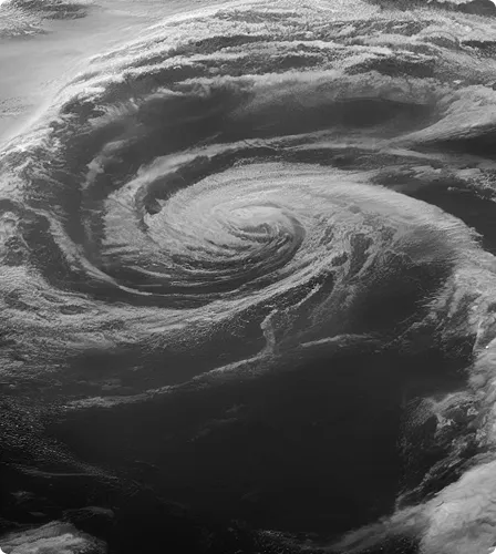 Black and white satellite image of a swirling hurricane over the ocean.