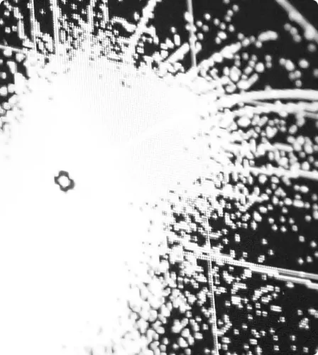 Close-up of a white pixelated explosion or light burst pattern on a black background.