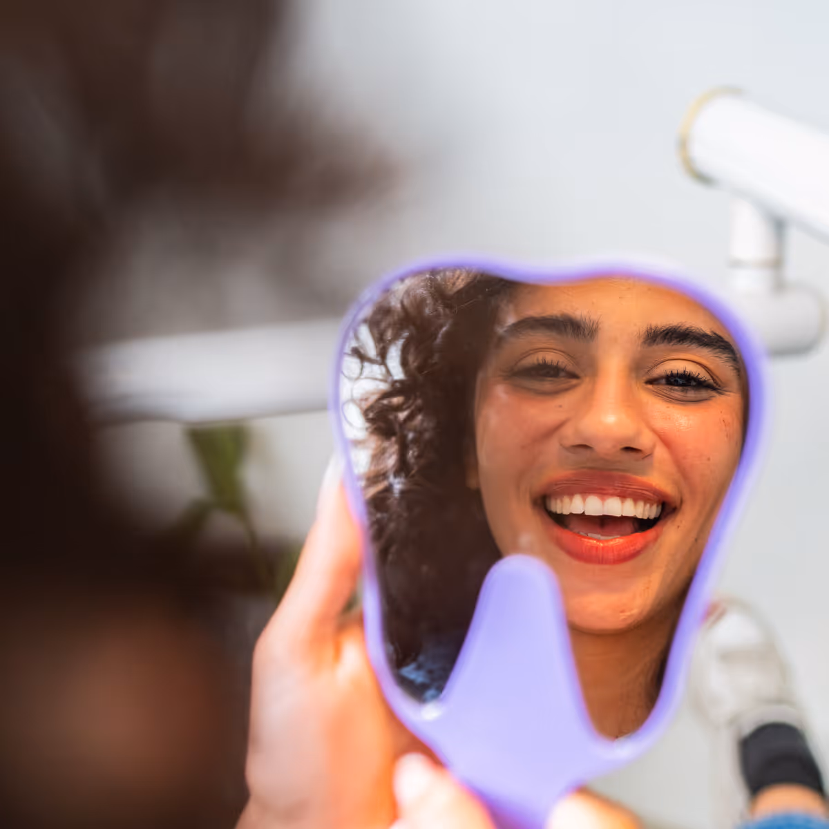 Dental patient looking at teeth in mirror after orthodontics