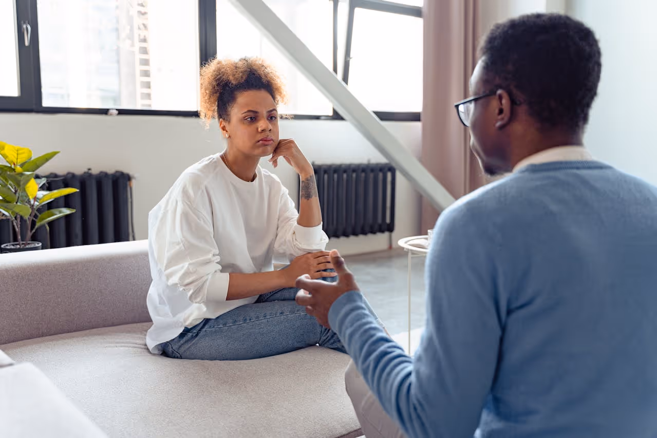 Young woman attentively listening to a man who is speaking during a counseling session in a bright room.