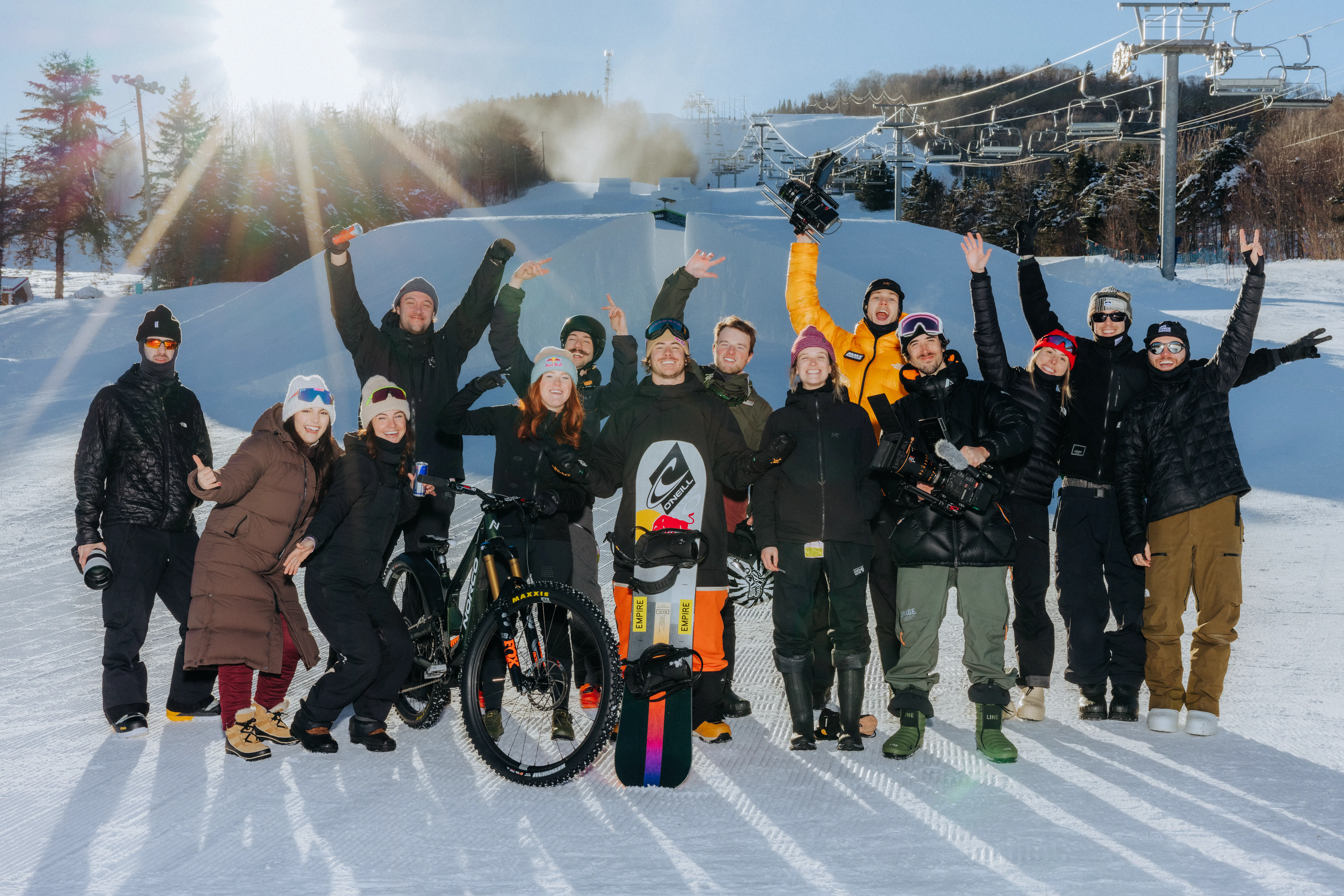 Groupe souriant en vêtements d'hiver posant sur la neige avec vélo et planche à neige au soleil.