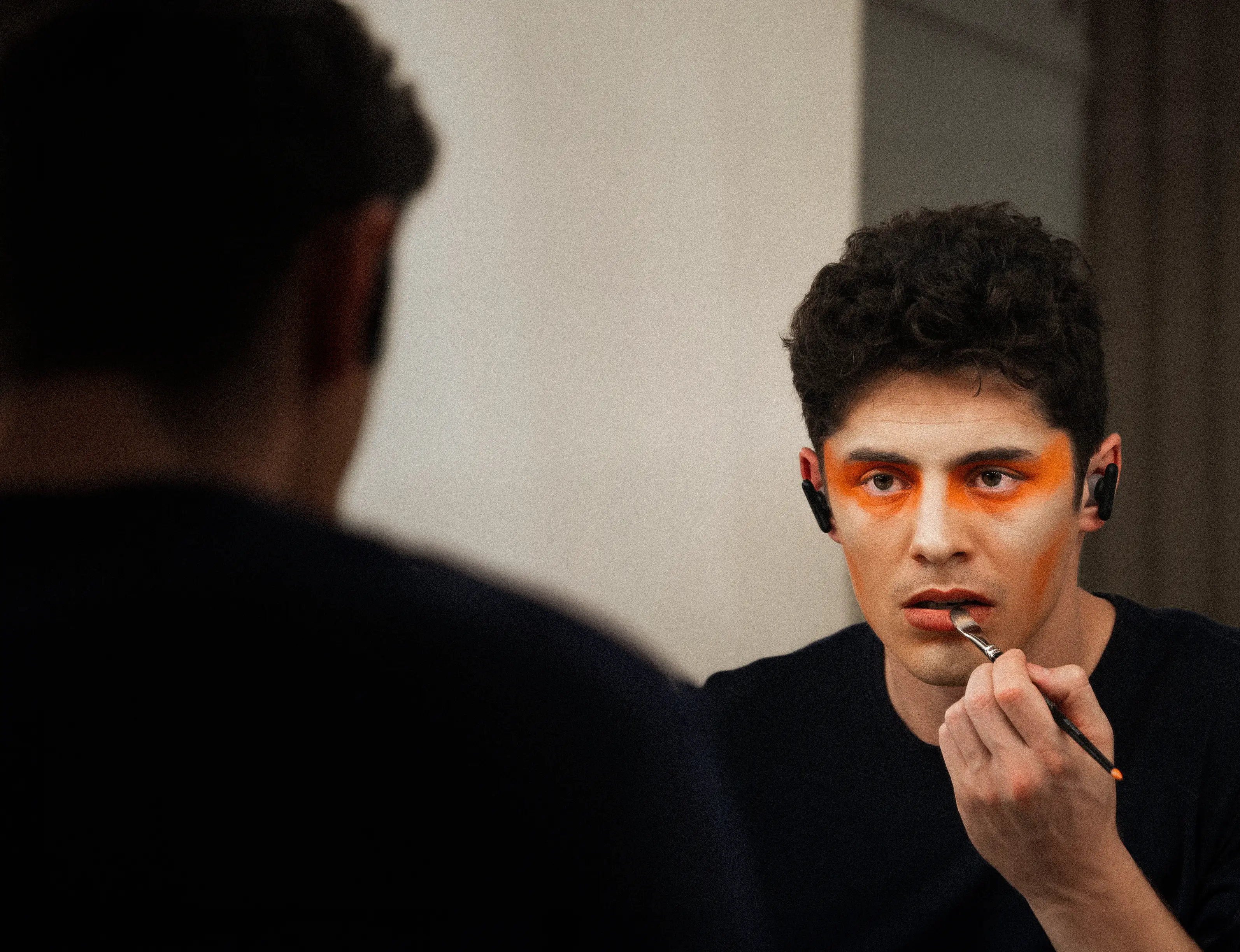 Un artiste du Cirque du Soleil appliquant du maquillage orange autour des yeux et sur les lèvres devant un miroir.