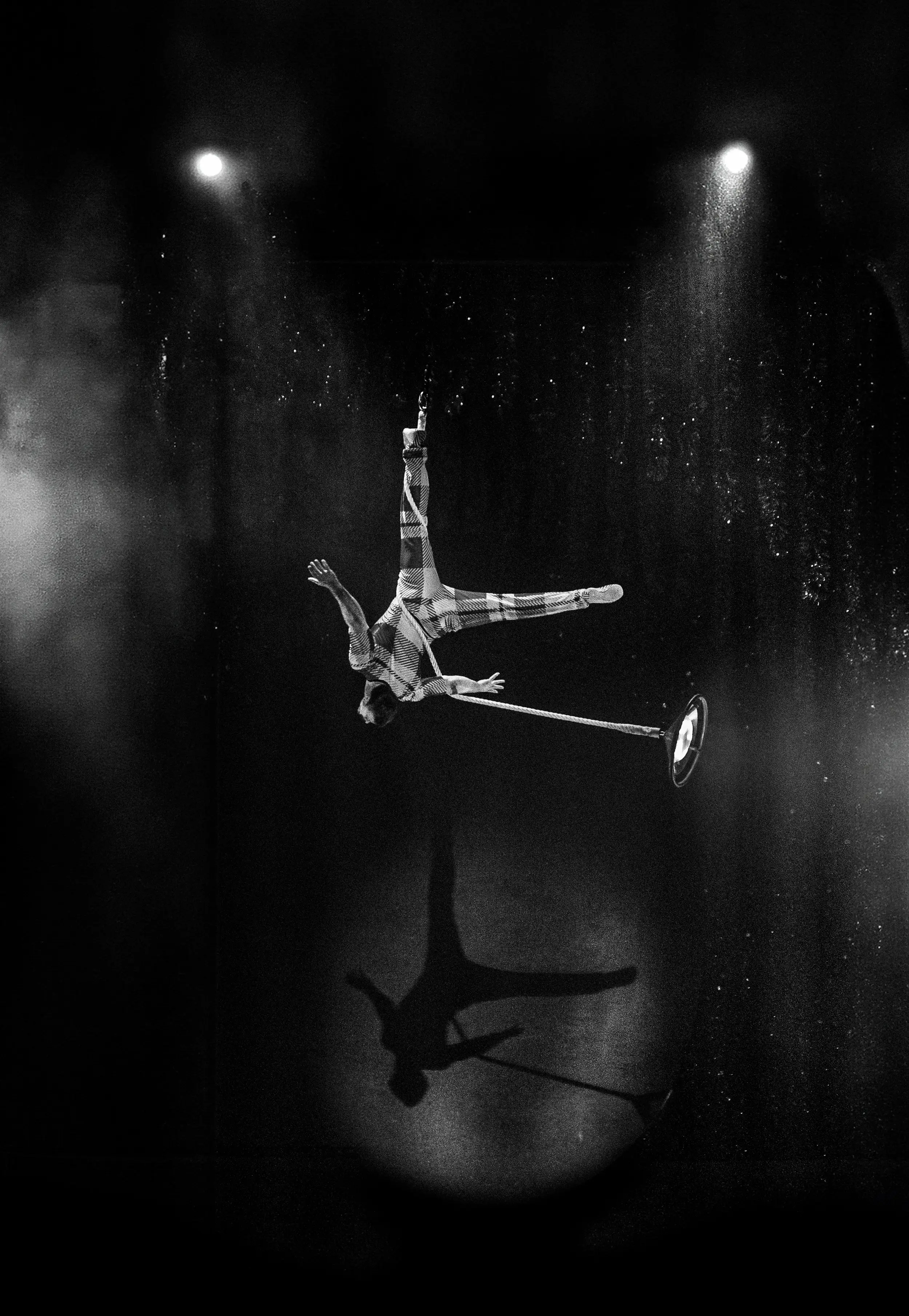 Acrobate du Cirque du Soleil suspendu en costume rayé lors d’une performance en hauteur avec un éclairage dramatique.