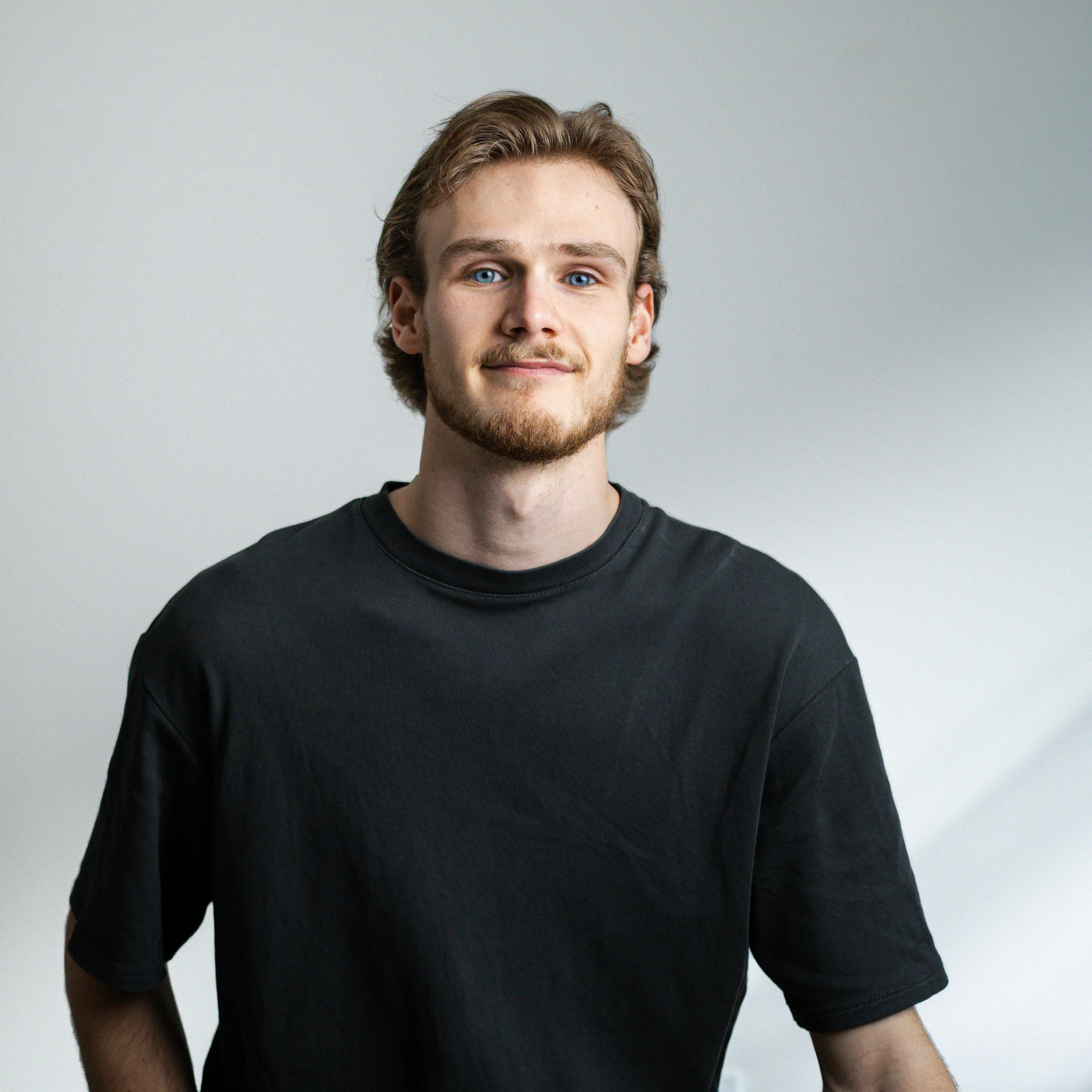 Portrait en noir et blanc de Justin Desjardins souriant avec t-shirt sombre sur fond uni clair.