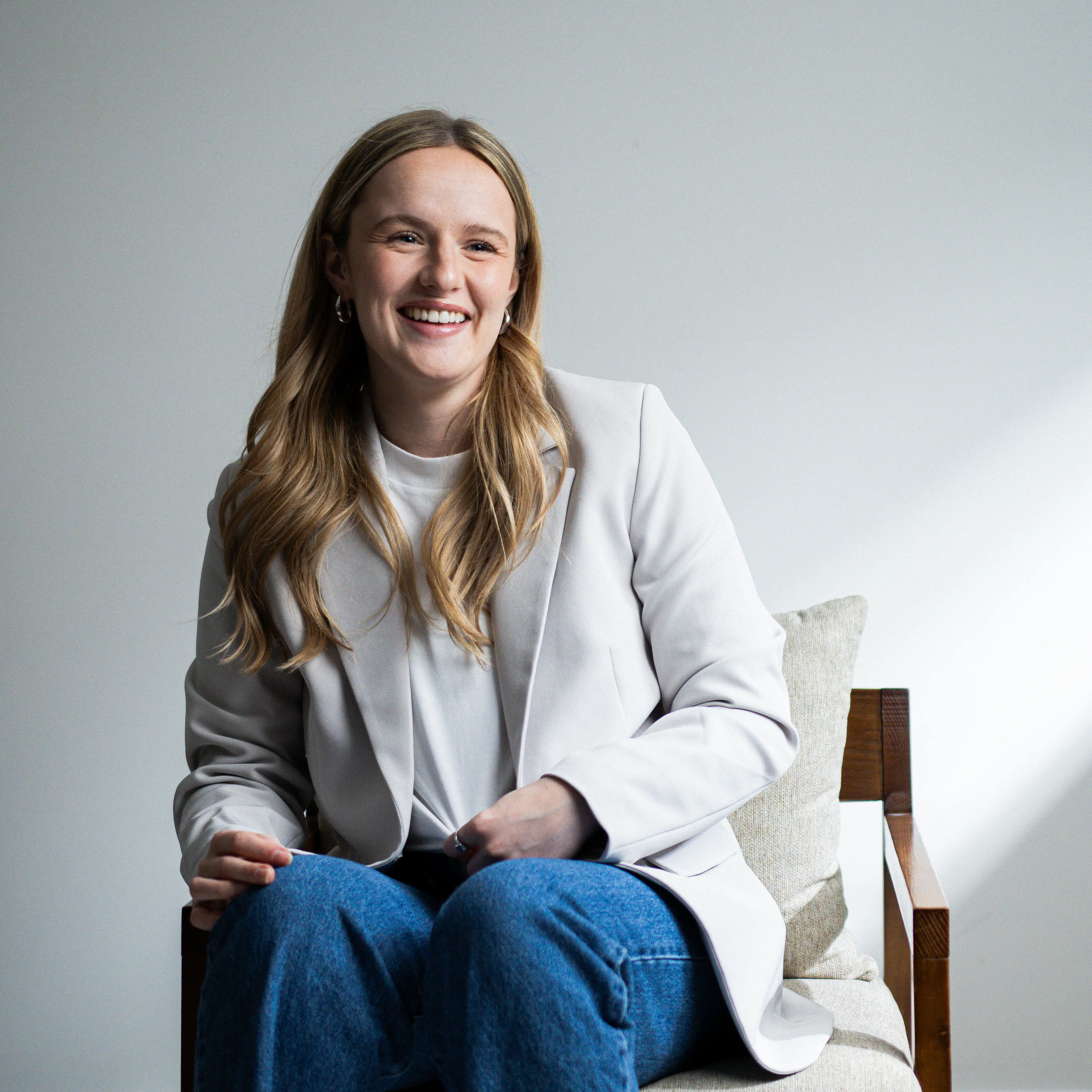 Portrait en noir et blanc de Sandrine Leclerc assise, souriant, portant un blazer clair et un jean.