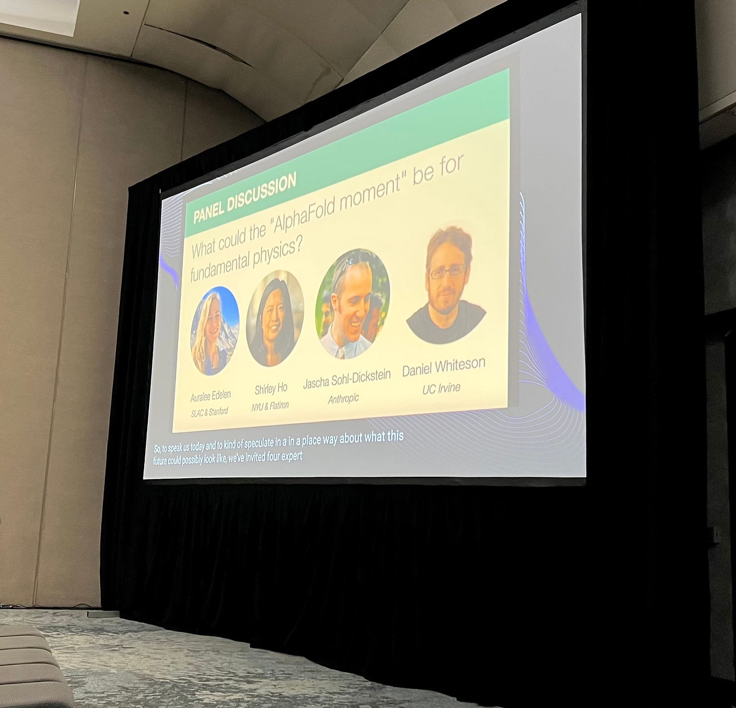 Panel discussion slide showing four speakers' photos under the topic "AlphaFold moment" in physics. Indoor setting with a dark curtain.