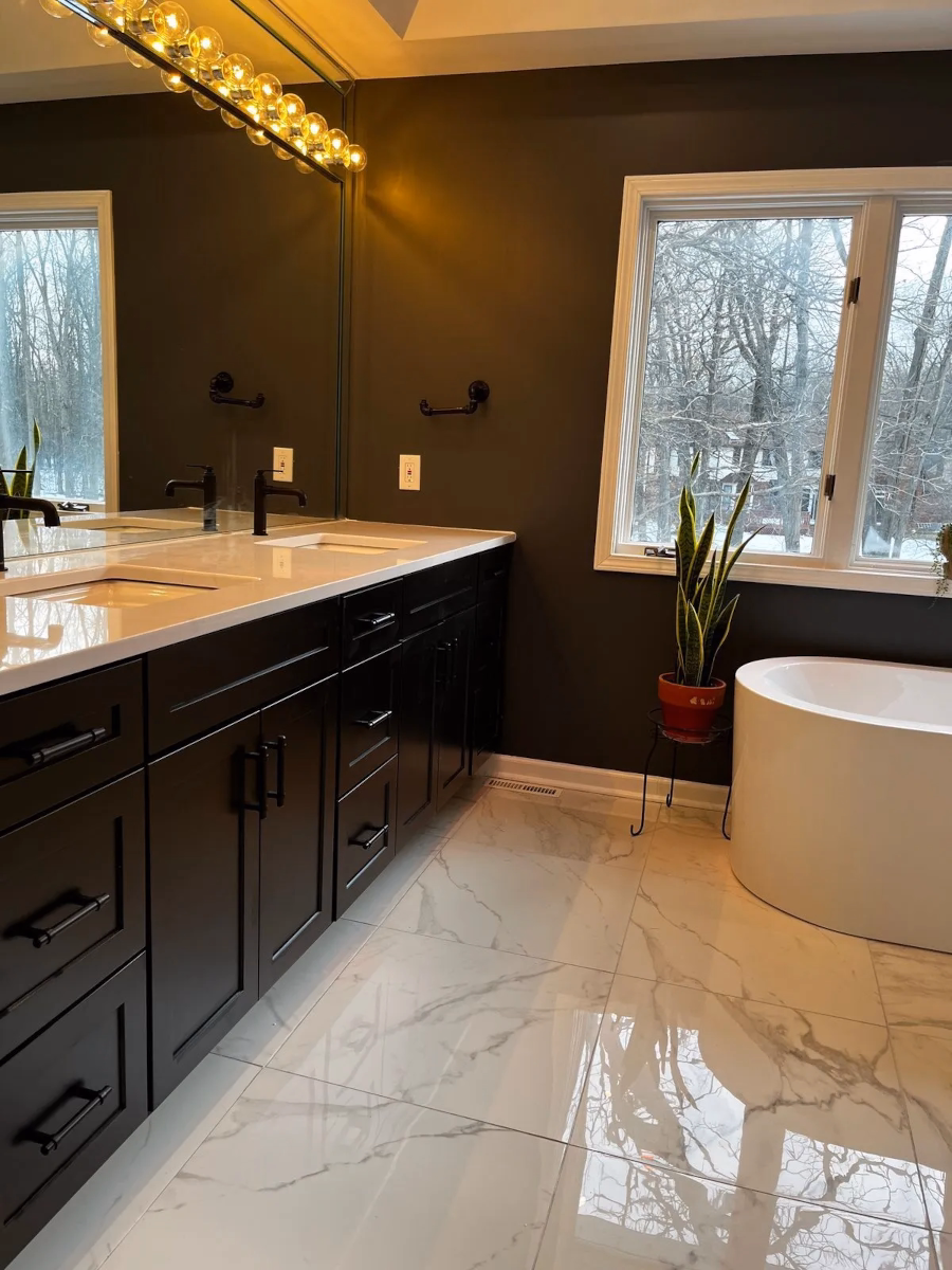 Remodeled bathroom with a black double vanity, marble-look tile floor and a freestanding soaking tub