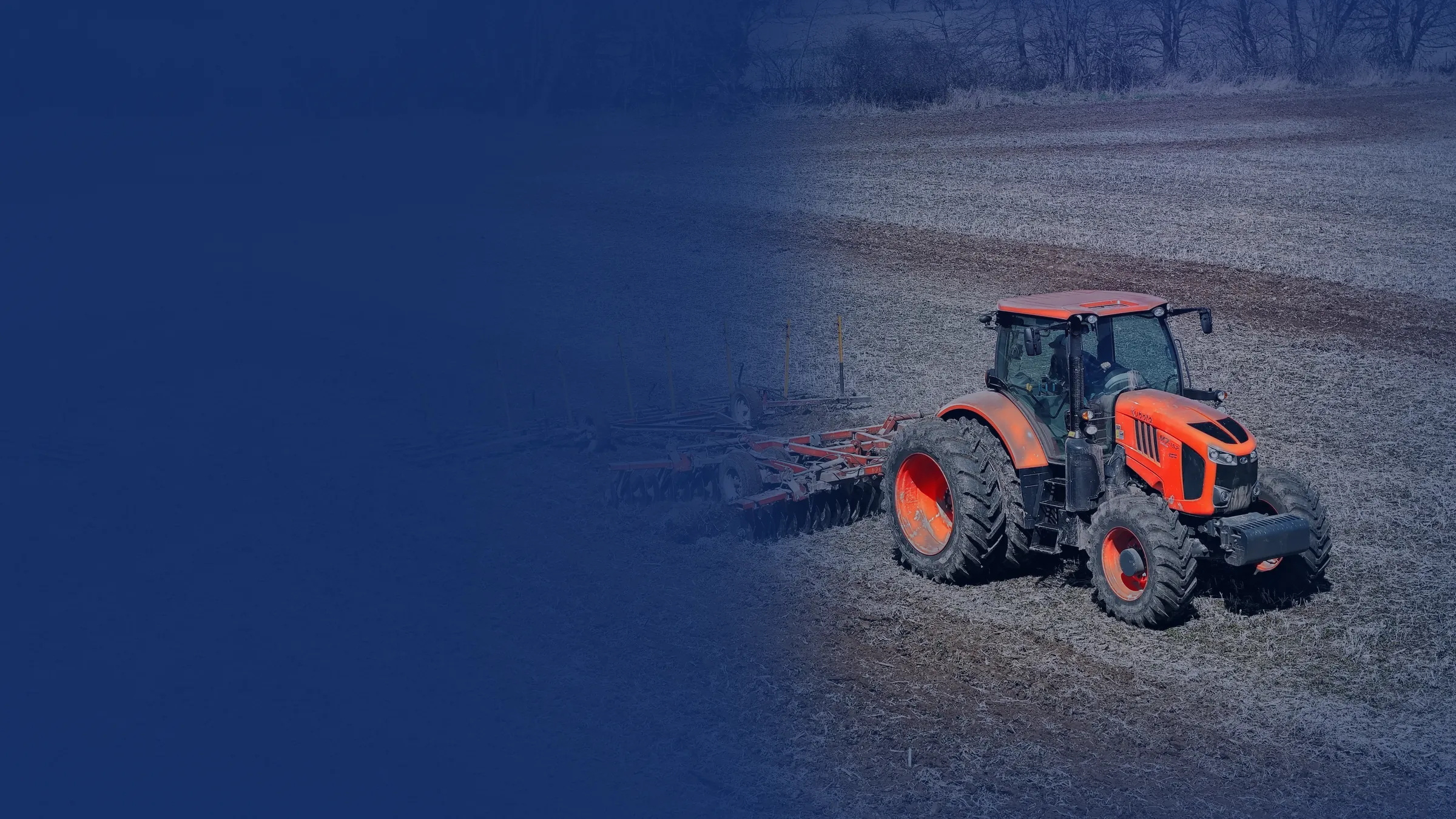 Kubota tractor pulling a disc harrow across a spring field