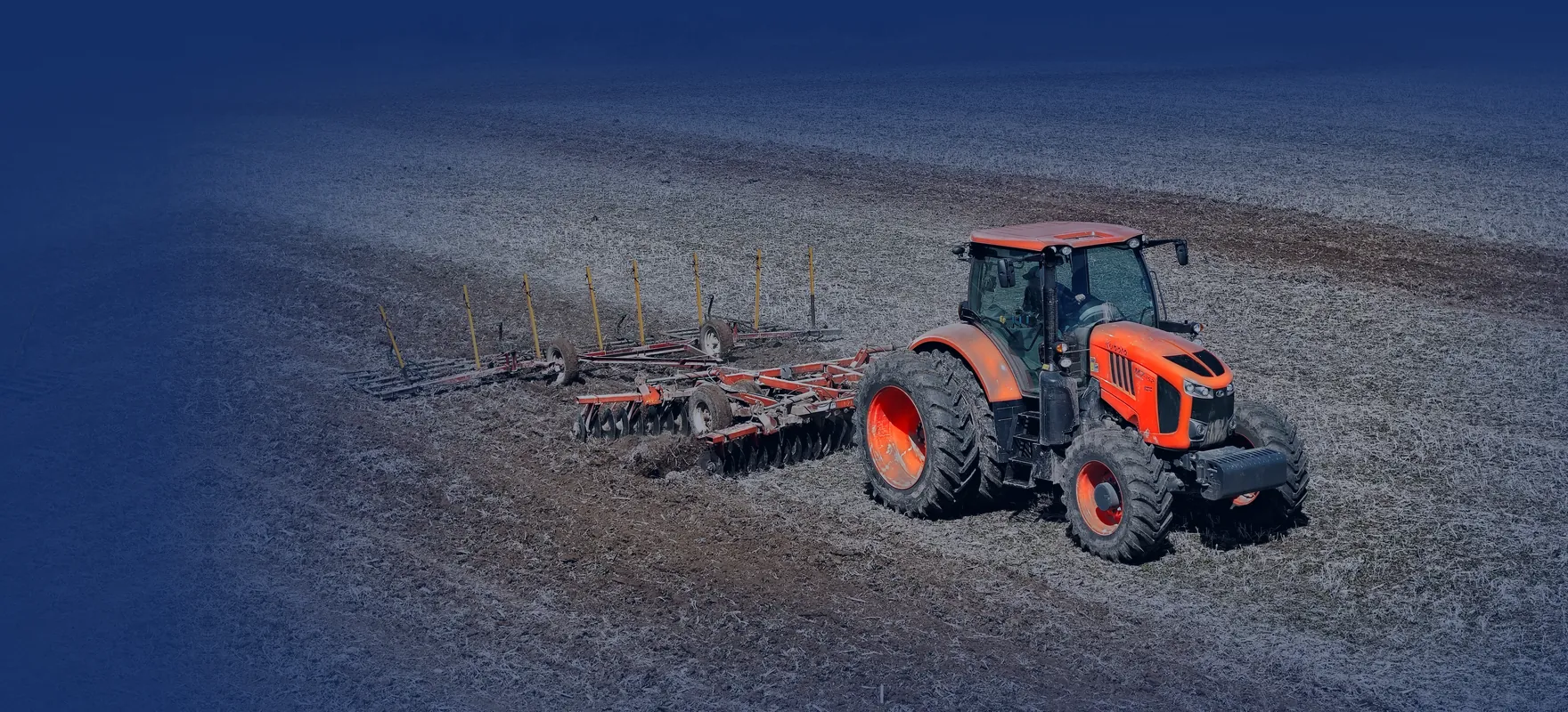 Kubota tractor pulling a disc harrow across a spring field