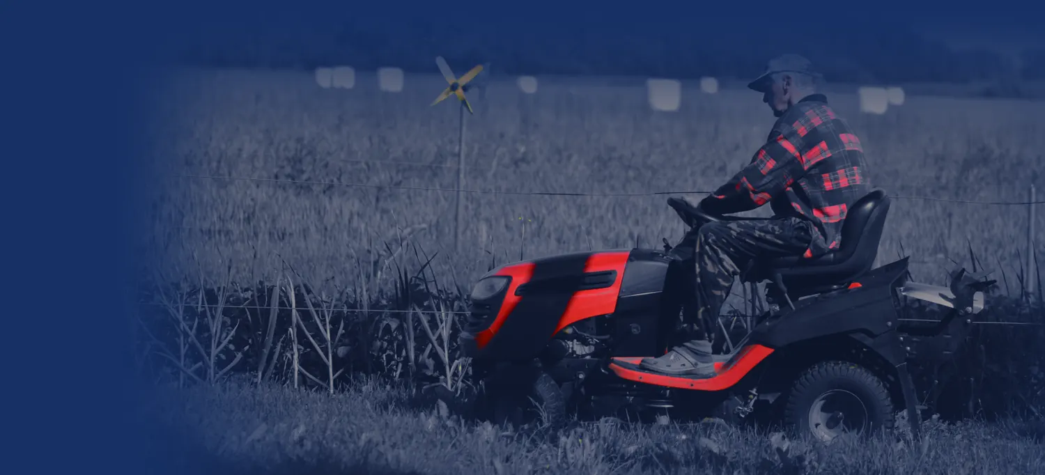 Operator on a red riding mower beside a farm field