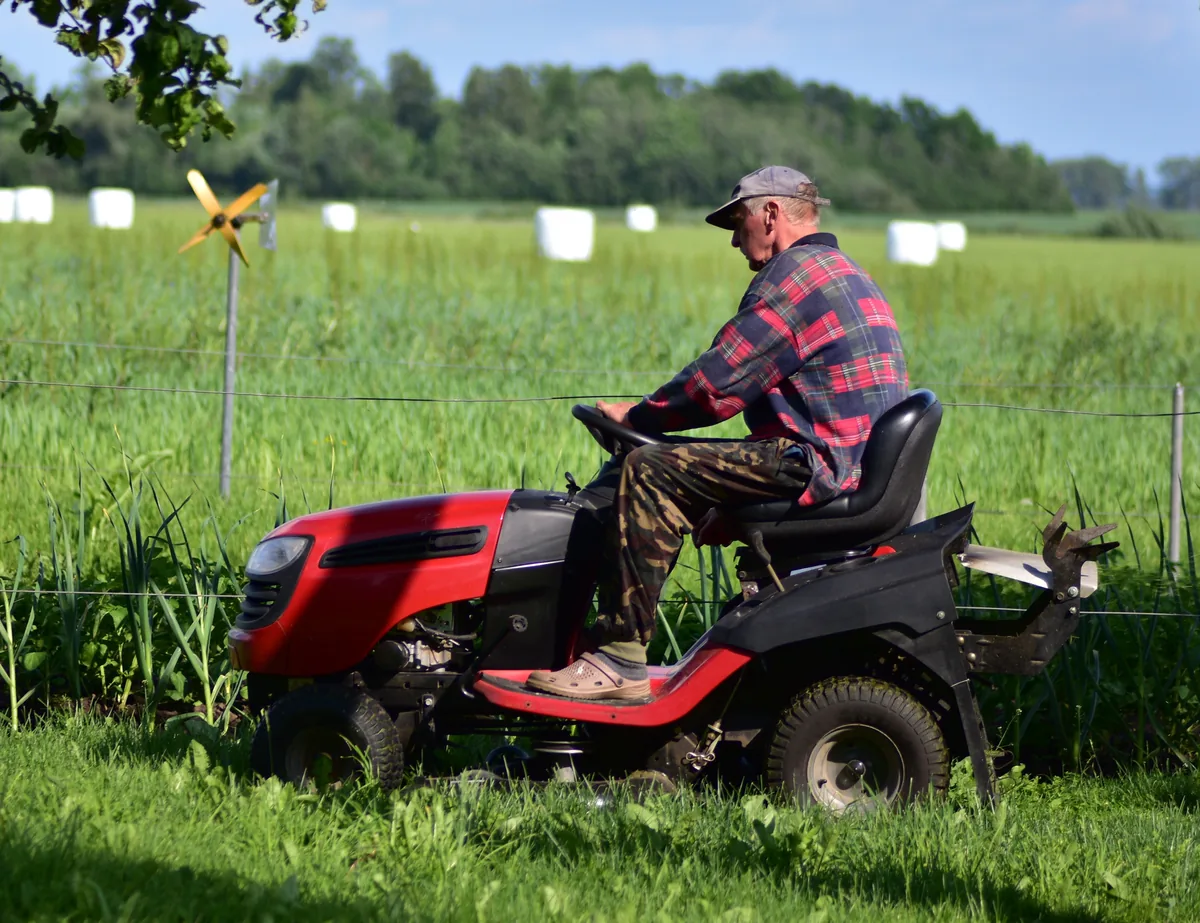 Operator mowing a farm lawn on a red riding mower