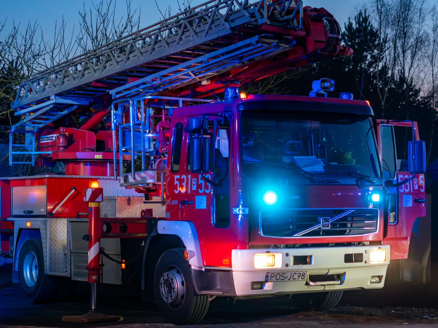 Volvo FL fire truck with an aerial ladder and emergency lights at dusk