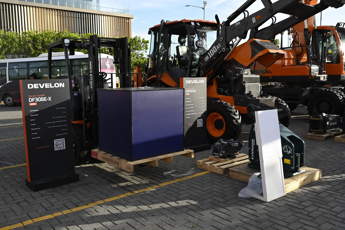 Develon DF30BE-X electric forklift and DB100AS backhoe loader on display at an equipment show
