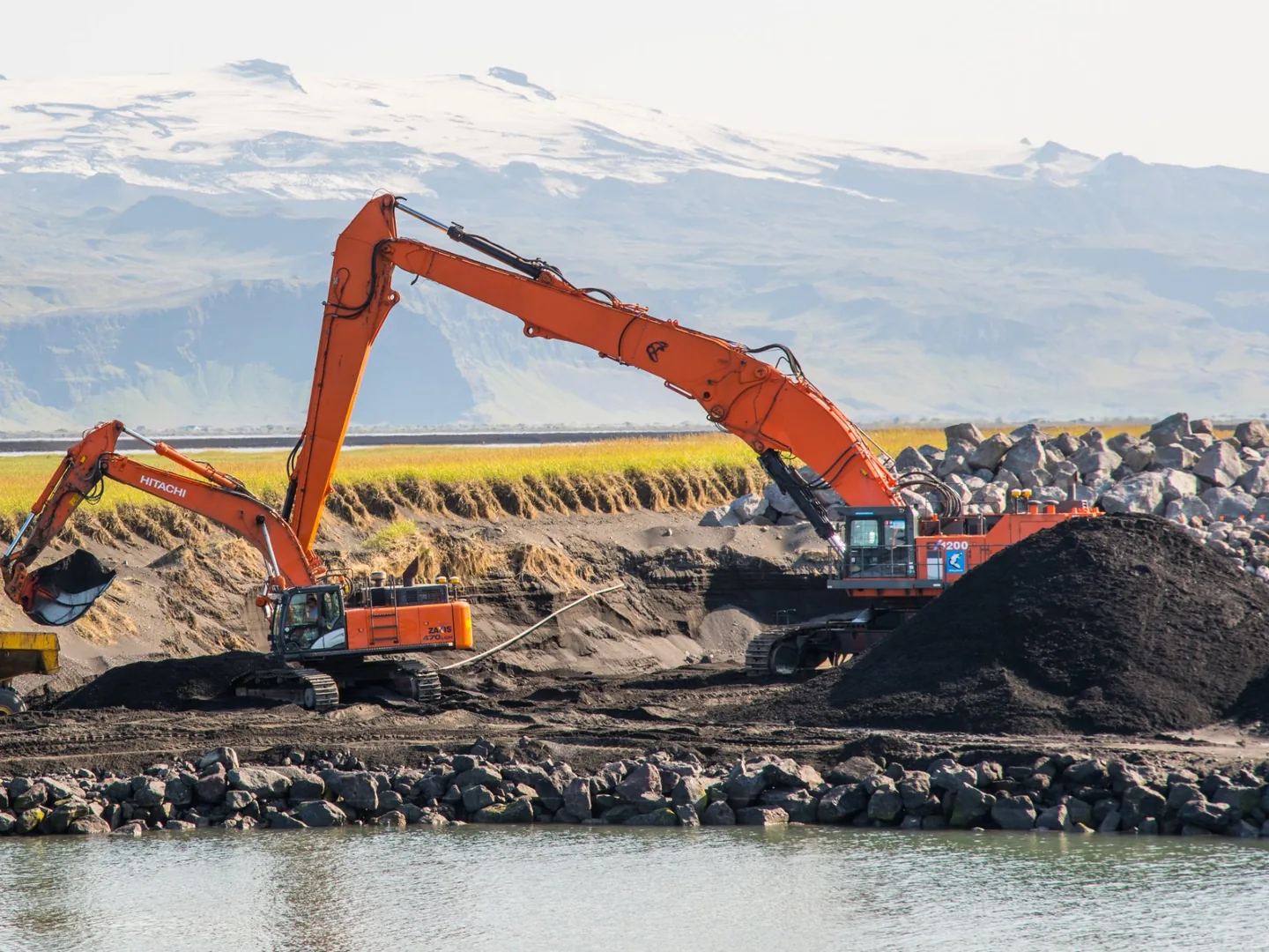 Hitachi ZX470LCH excavator loading a haul truck beside a river, with a larger Hitachi excavator behind it