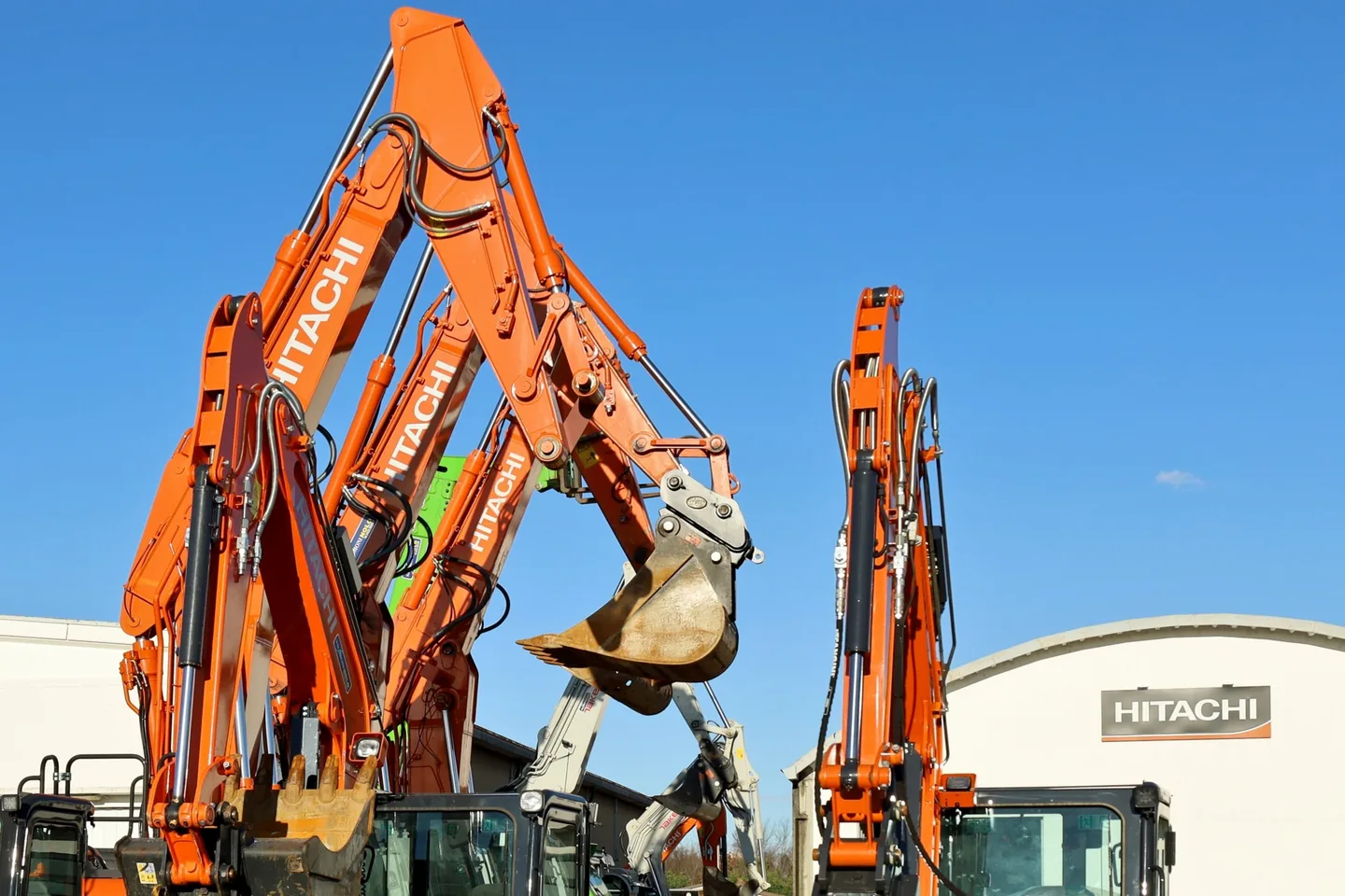 Hitachi excavators with booms raised outside a Hitachi dealership building