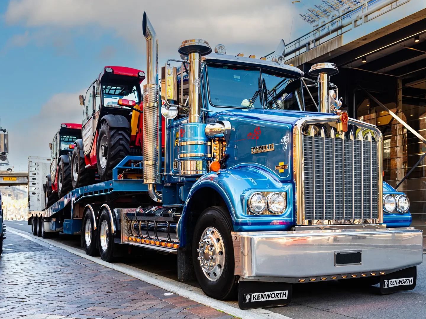 Blue Kenworth truck hauling two telehandlers on a trailer